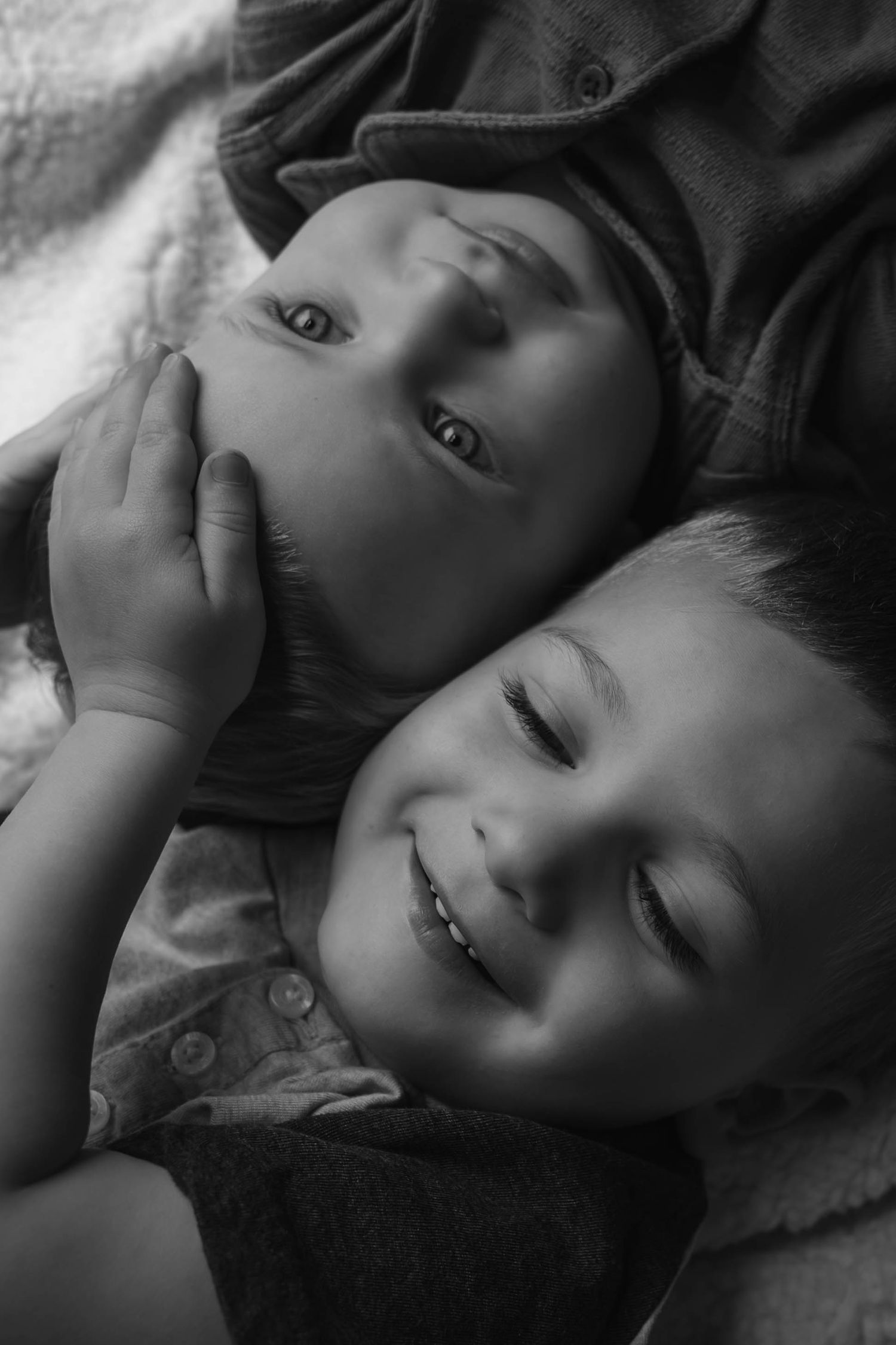 Black and white close-up of two young brothers cuddling and smiling together on a blanket.