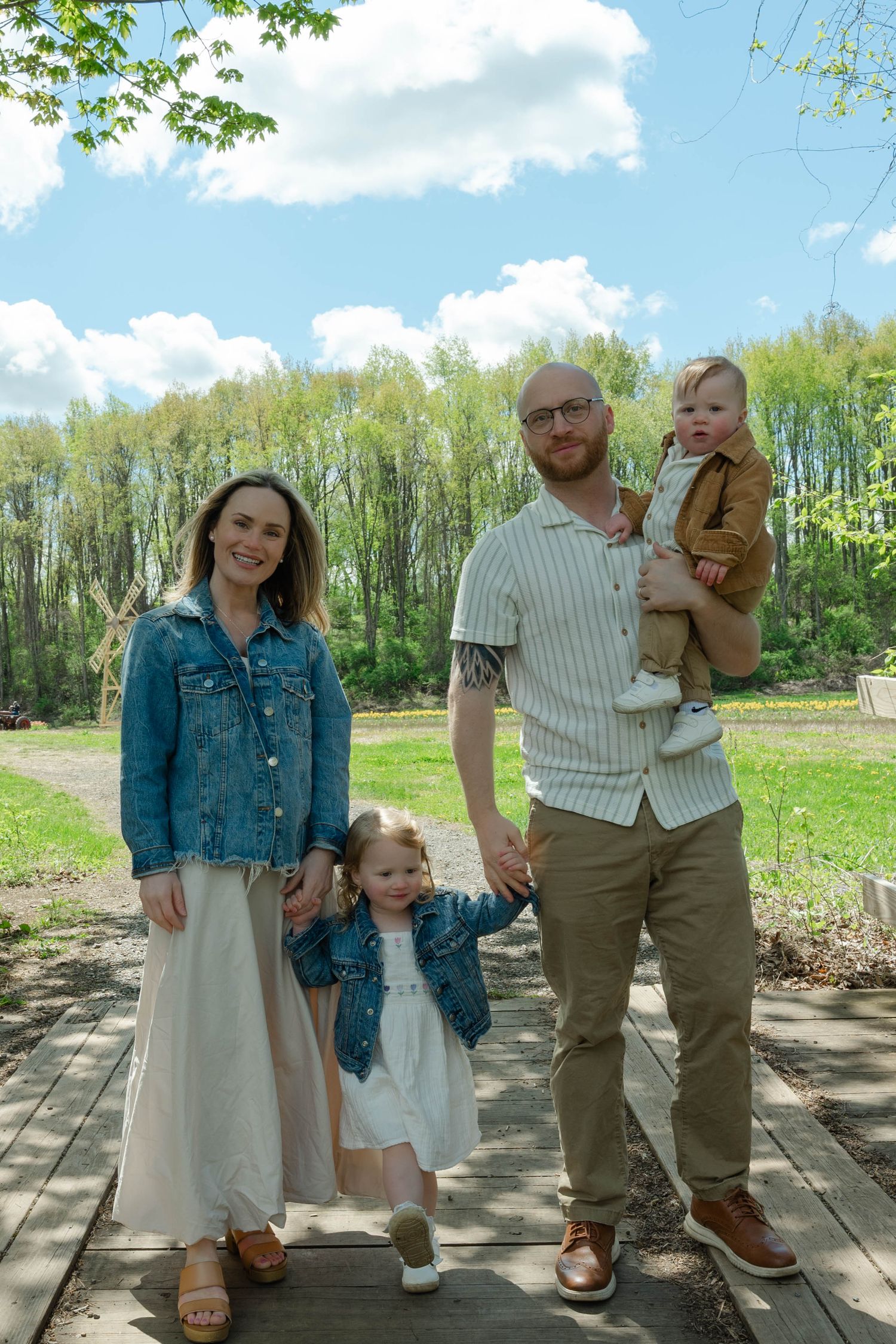 Family of four posing on a wooden path surrounded by lush green spring trees.