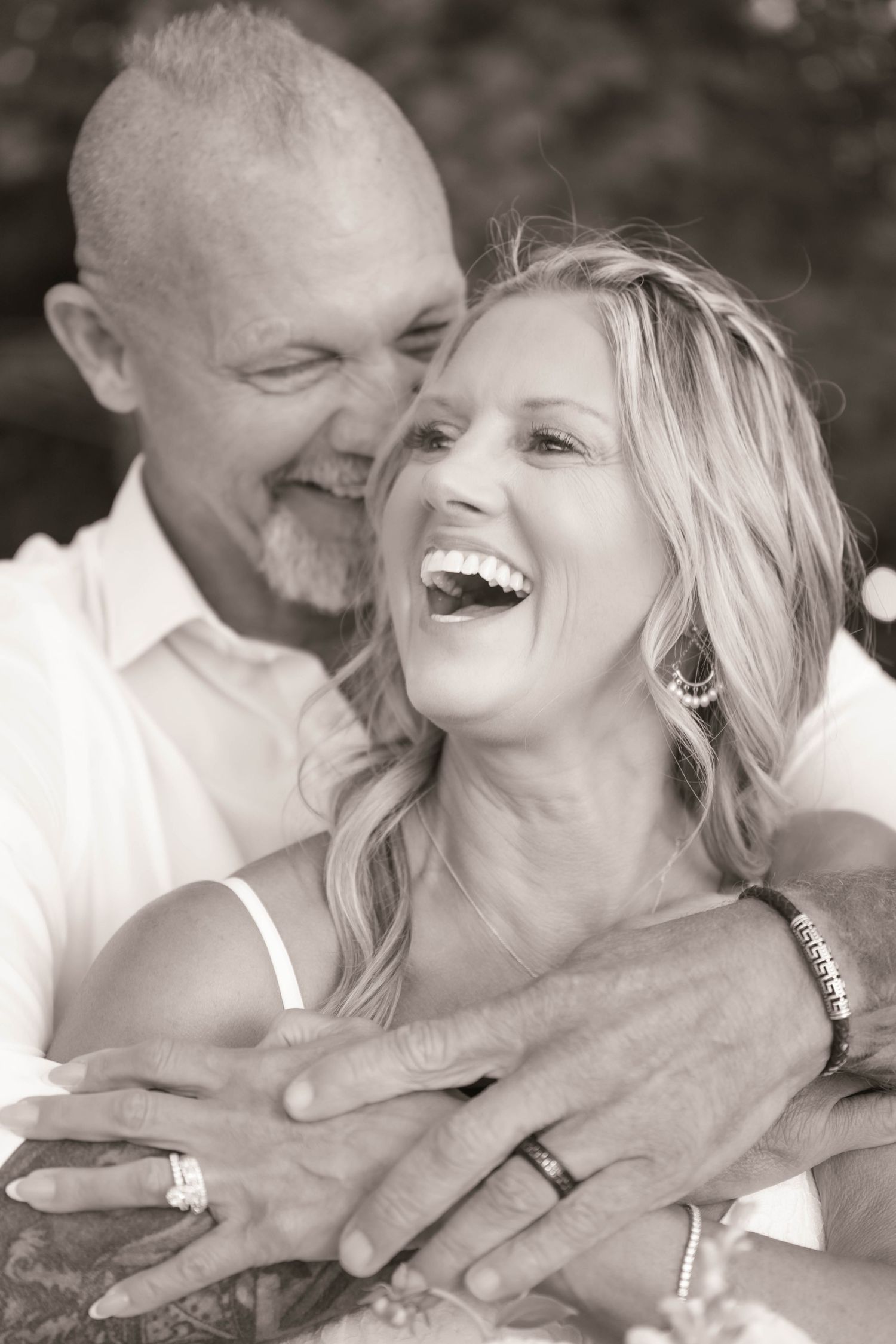 Black and white photo of a laughing couple embracing, showing wedding rings, capturing a joyful romantic moment.