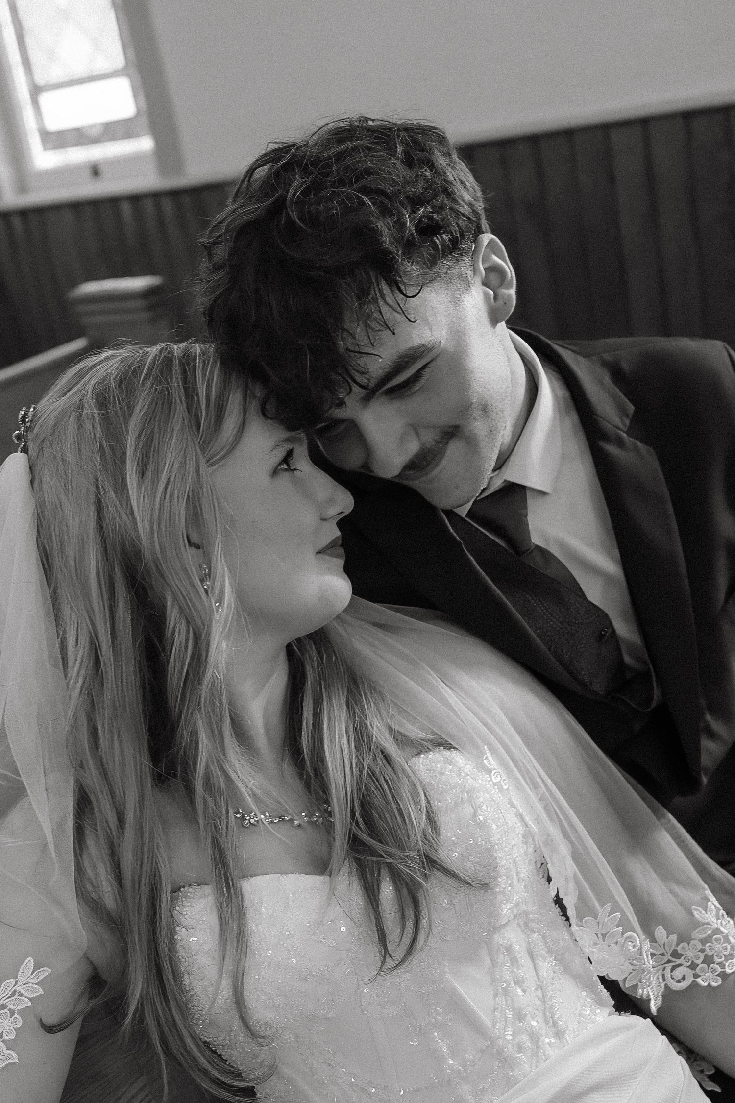 Black and white wedding photo of a smiling groom in a suit and bride in lace dress sharing a tender moment.