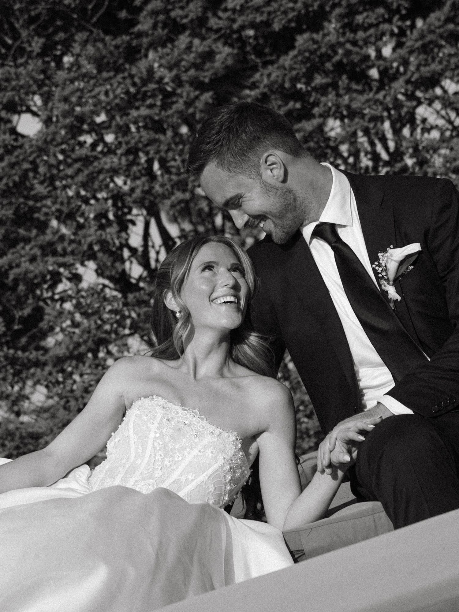 Black and white photo of laughing bride looking up at smiling groom on outdoor lounge.