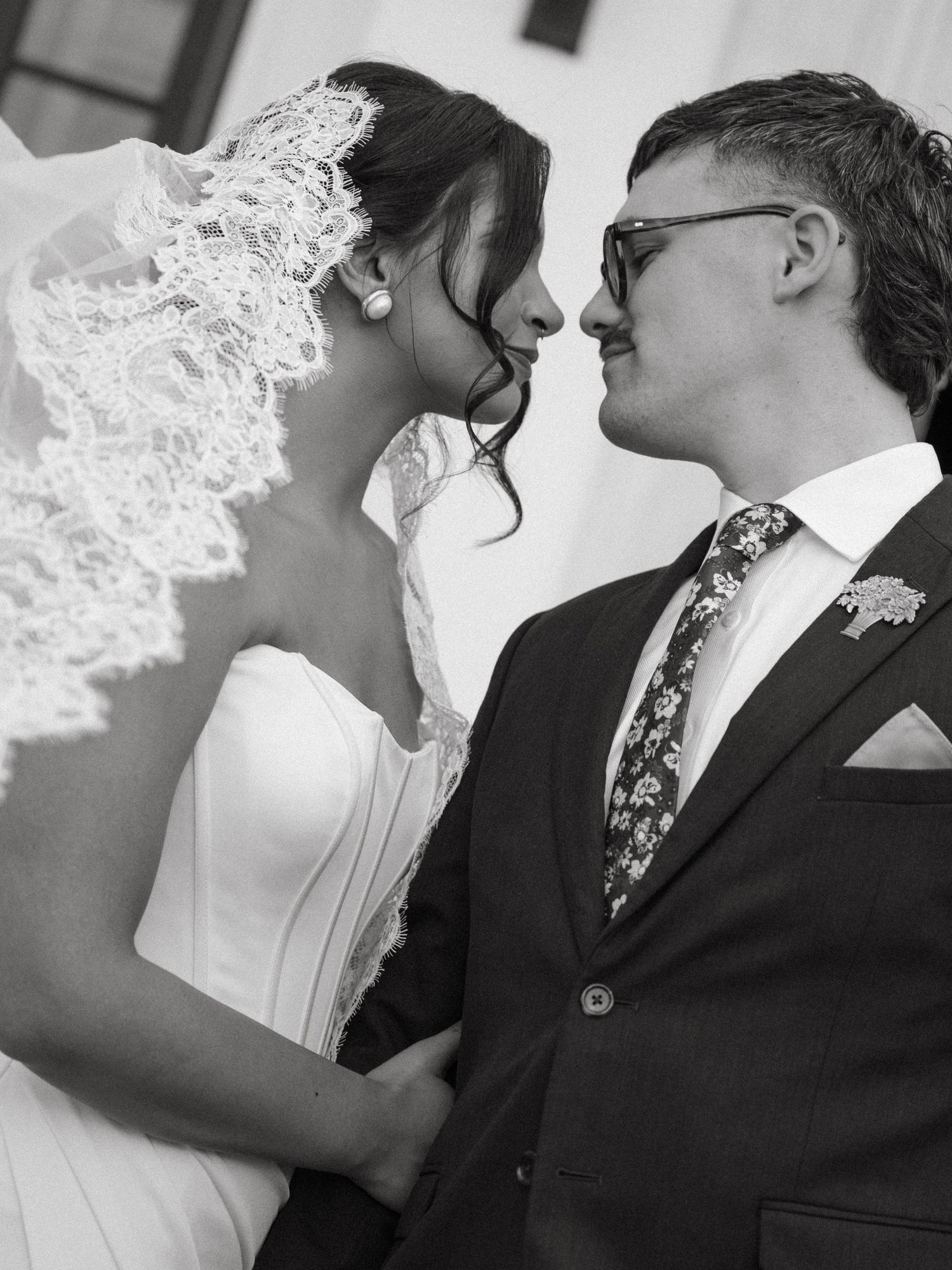 Black and white portrait of bride and groom sharing an intimate moment, bride wearing lace veil.