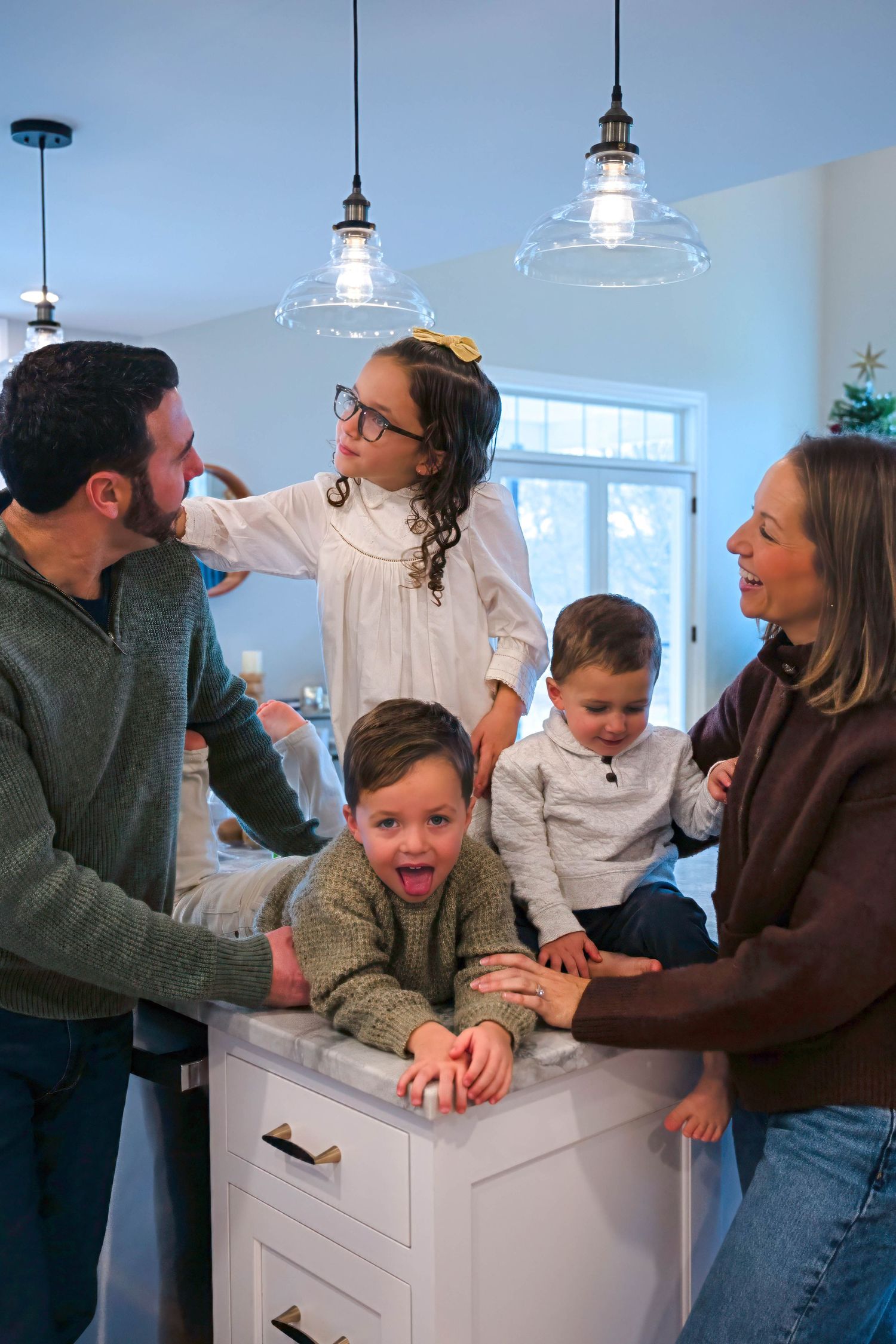 Joyful family gathering around white kitchen island with laughing child leaning on counter.