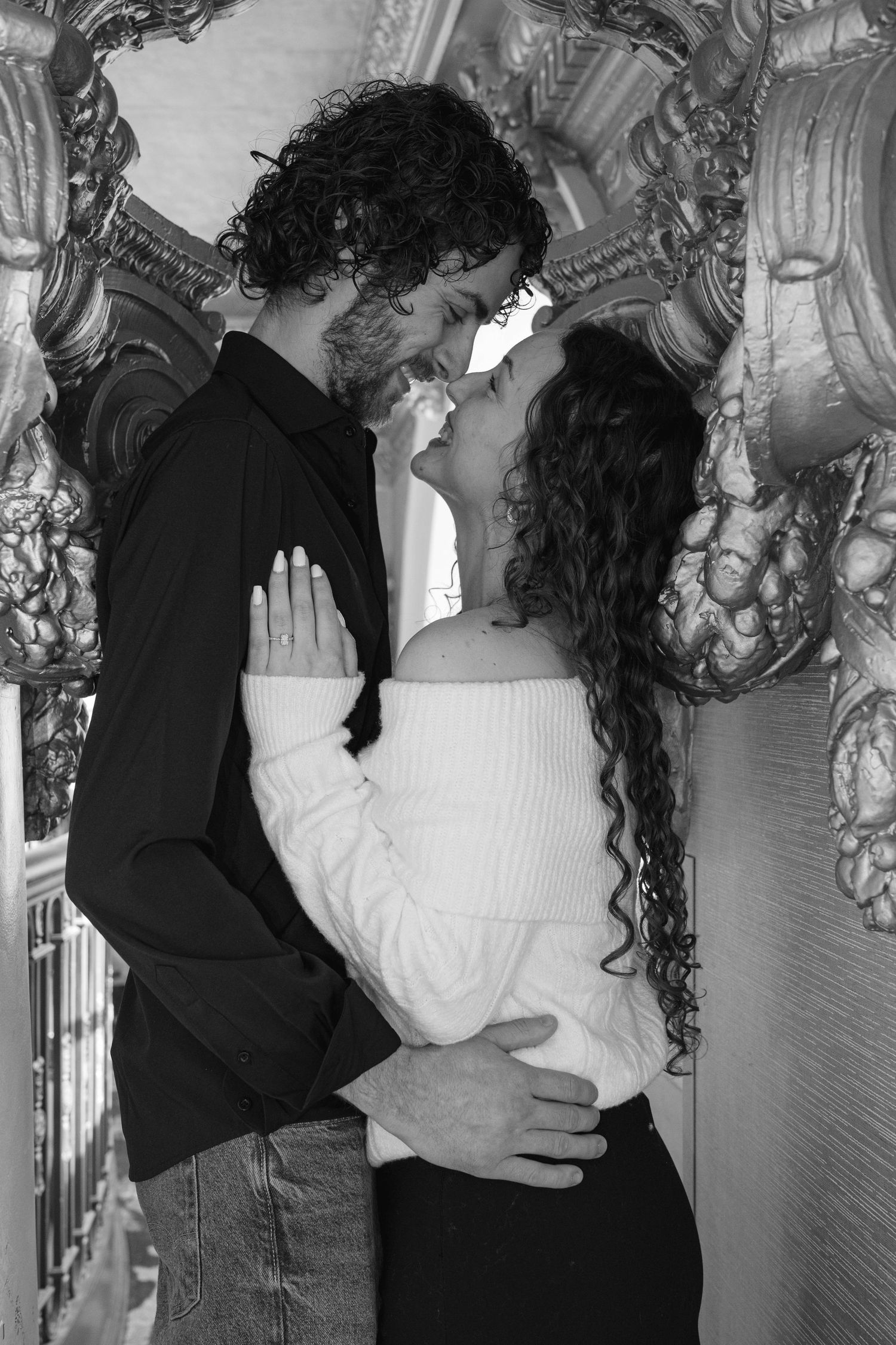 Black and white romantic portrait of couple nearly kissing framed by ornate baroque architectural details.