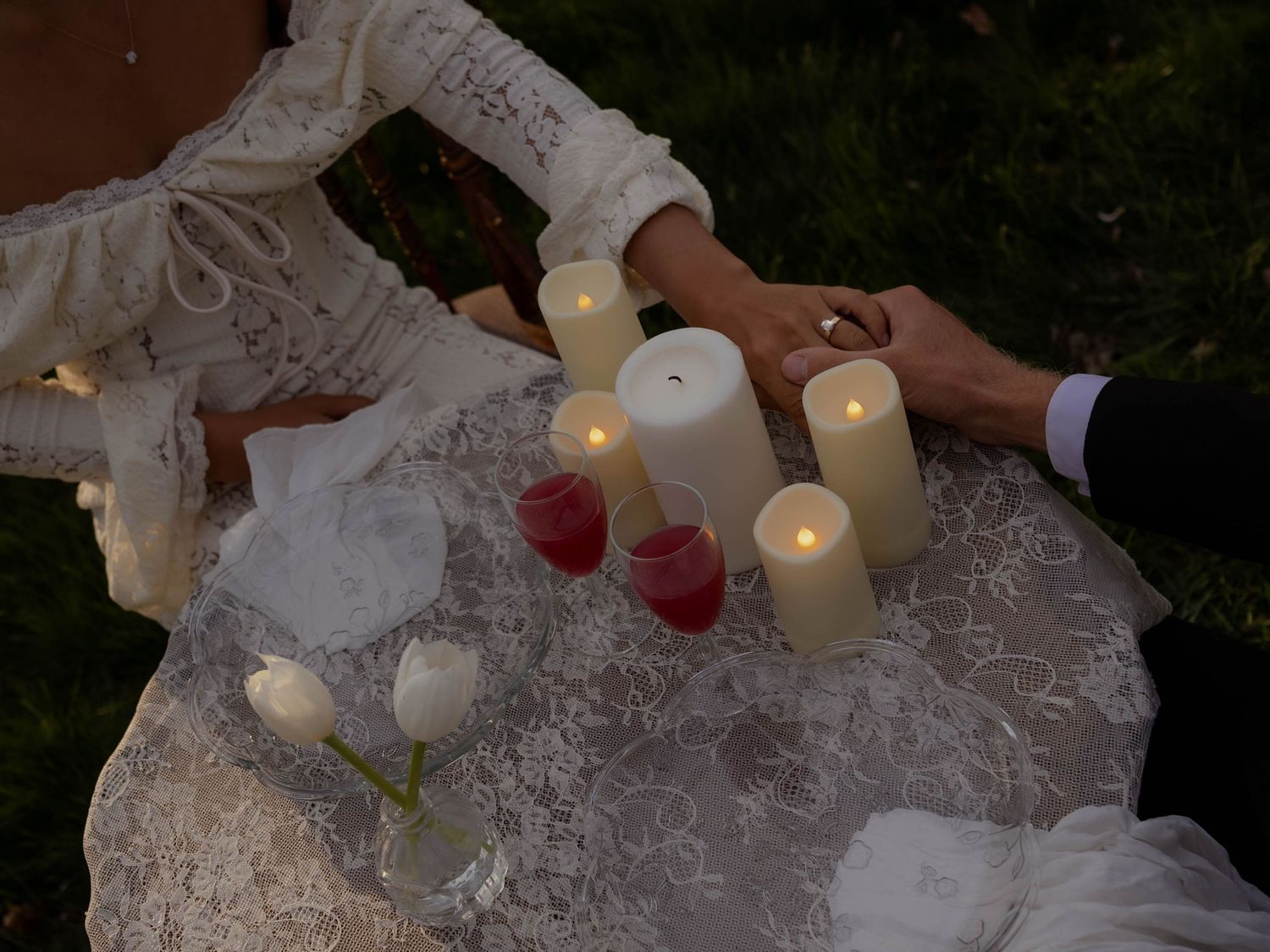 Overhead view of bride and groom holding hands over a table adorned with glowing candles.