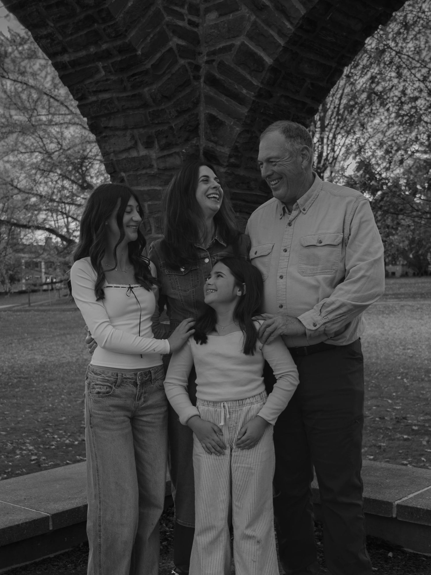 Black and white photo of a joyful family of four laughing together beneath a large stone arch.