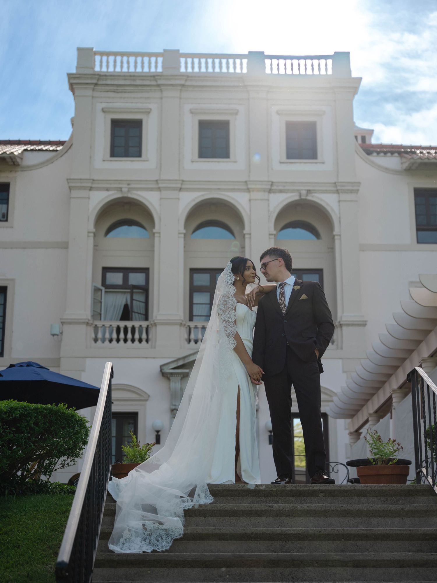 Newlyweds sharing an intimate moment on steps of a beautiful white neoclassical building on their wedding day.