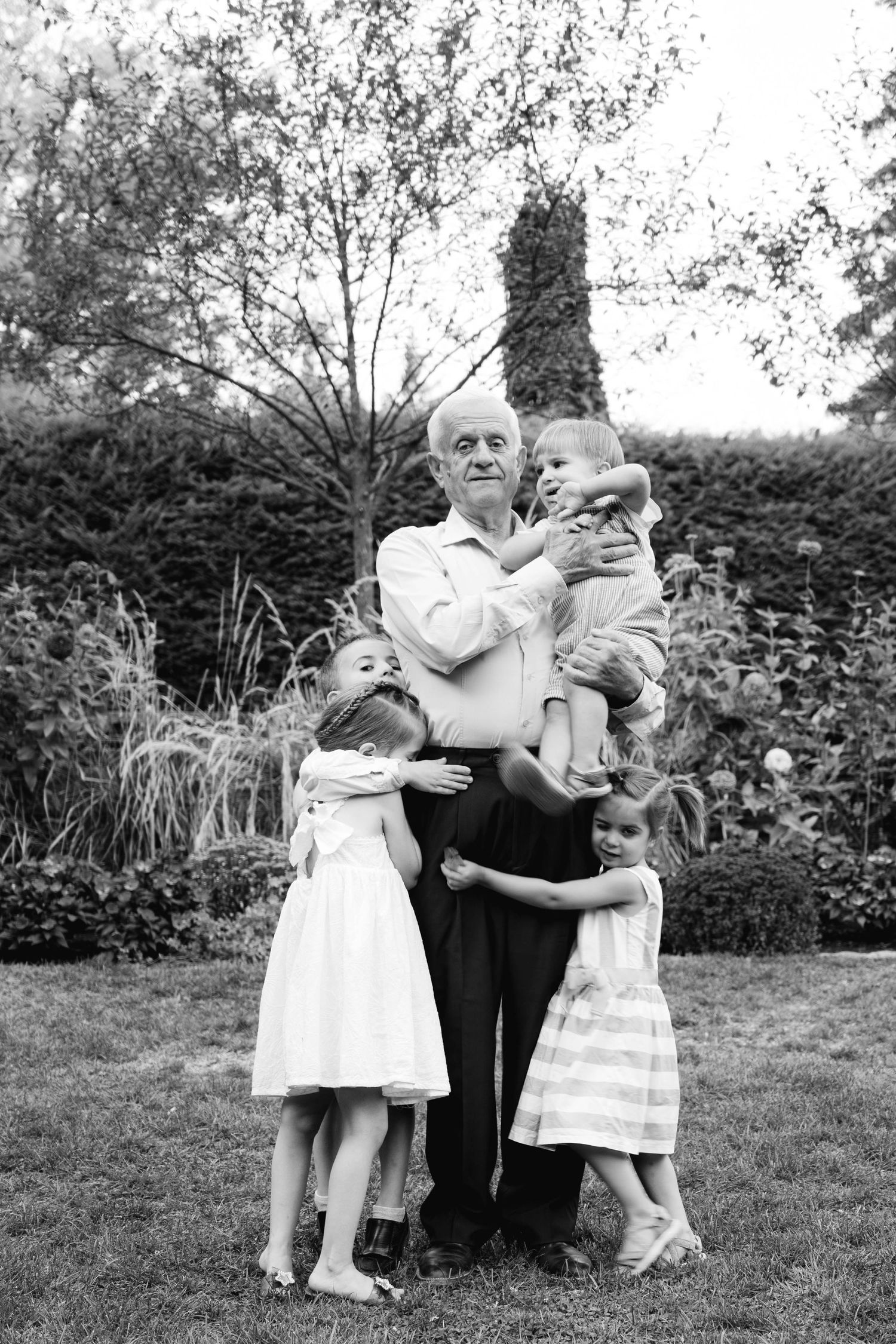 Black and white portrait of grandfather embracing four grandchildren in a garden, capturing a tender family moment.