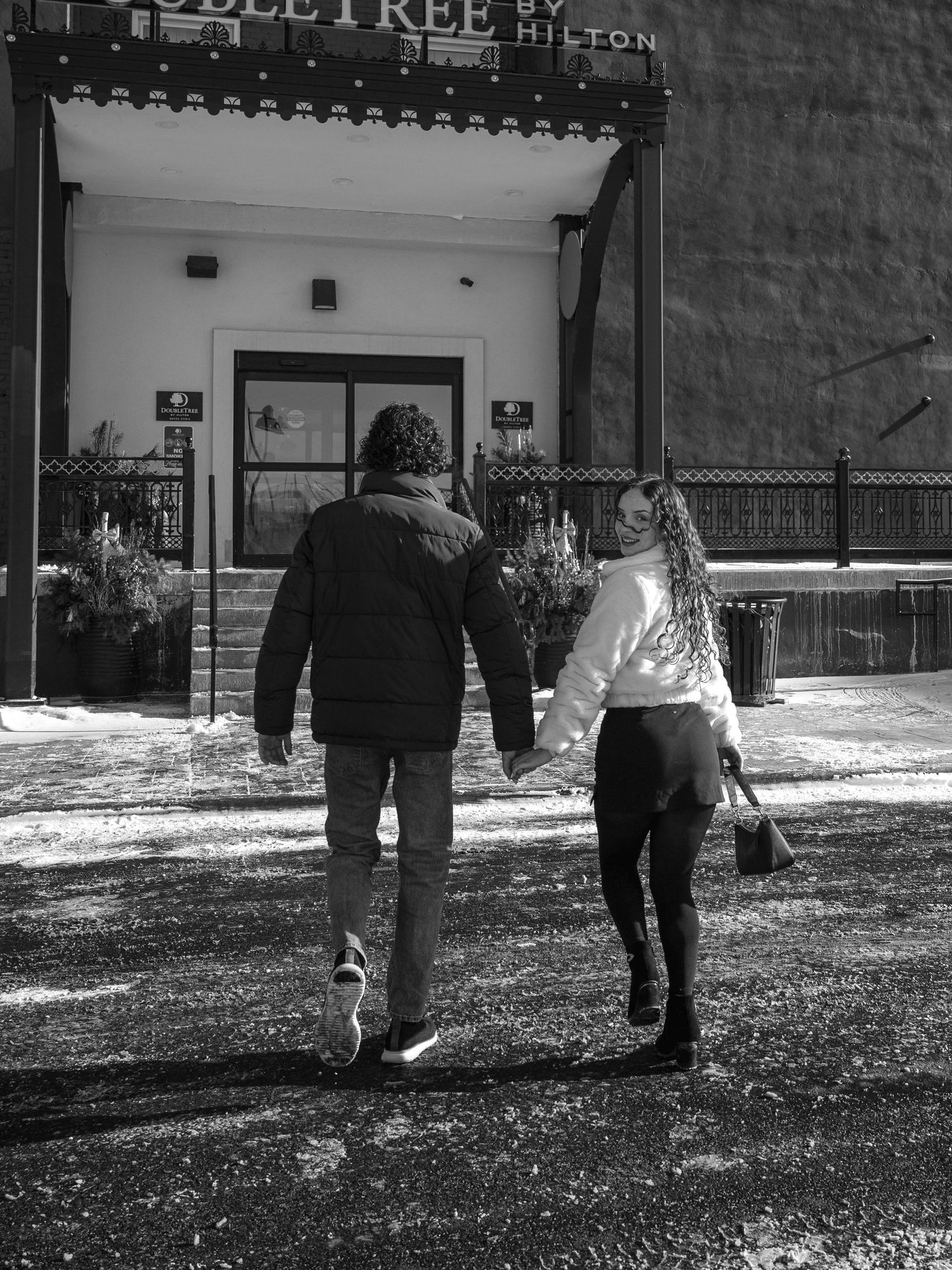 Black and white photo of couple walking hand in hand toward a DoubleTree by Hilton hotel entrance.