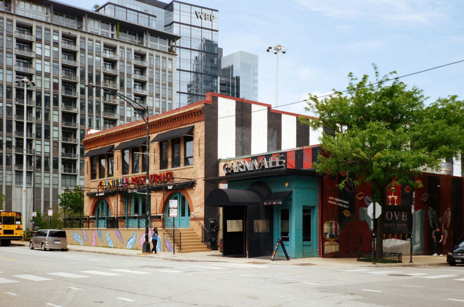 Colorful urban street corner with low-rise brick buildings and modern skyscrapers in the background on a sunny day.