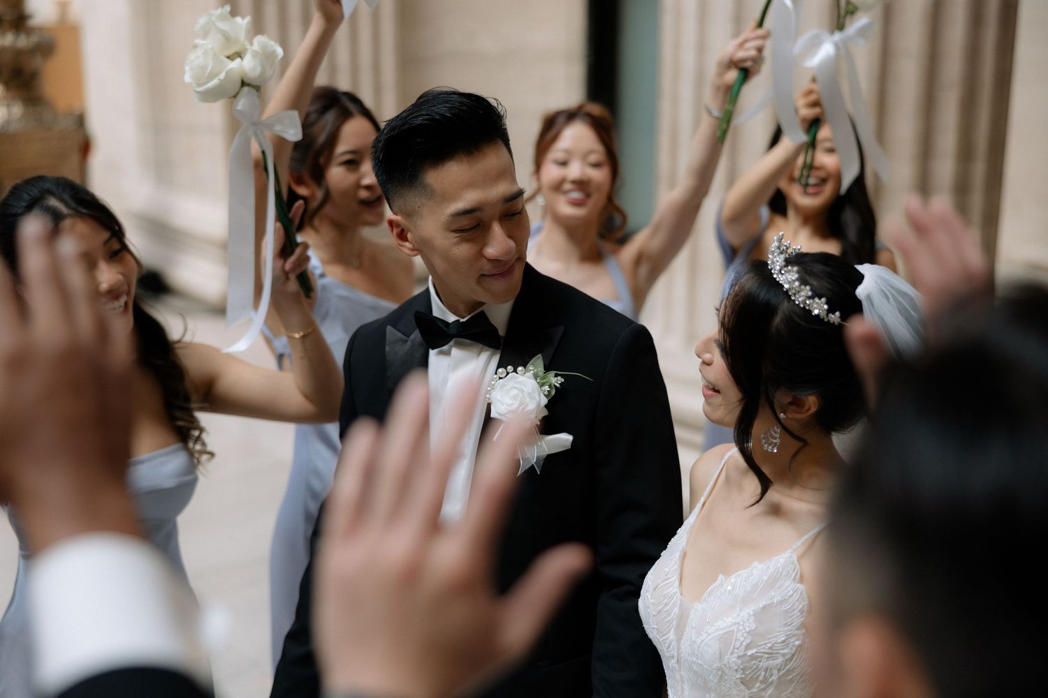 Joyful bride and groom celebrated by bridesmaids in light blue dresses waving white floral wands.
