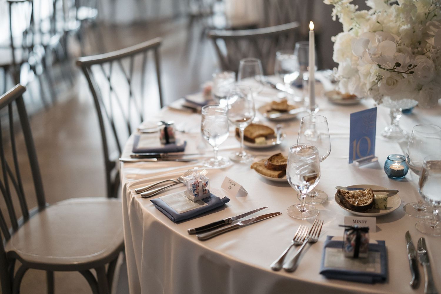 Elegant wedding reception table setting with white linens, crystal glassware, floral centerpiece, and navy blue place cards.