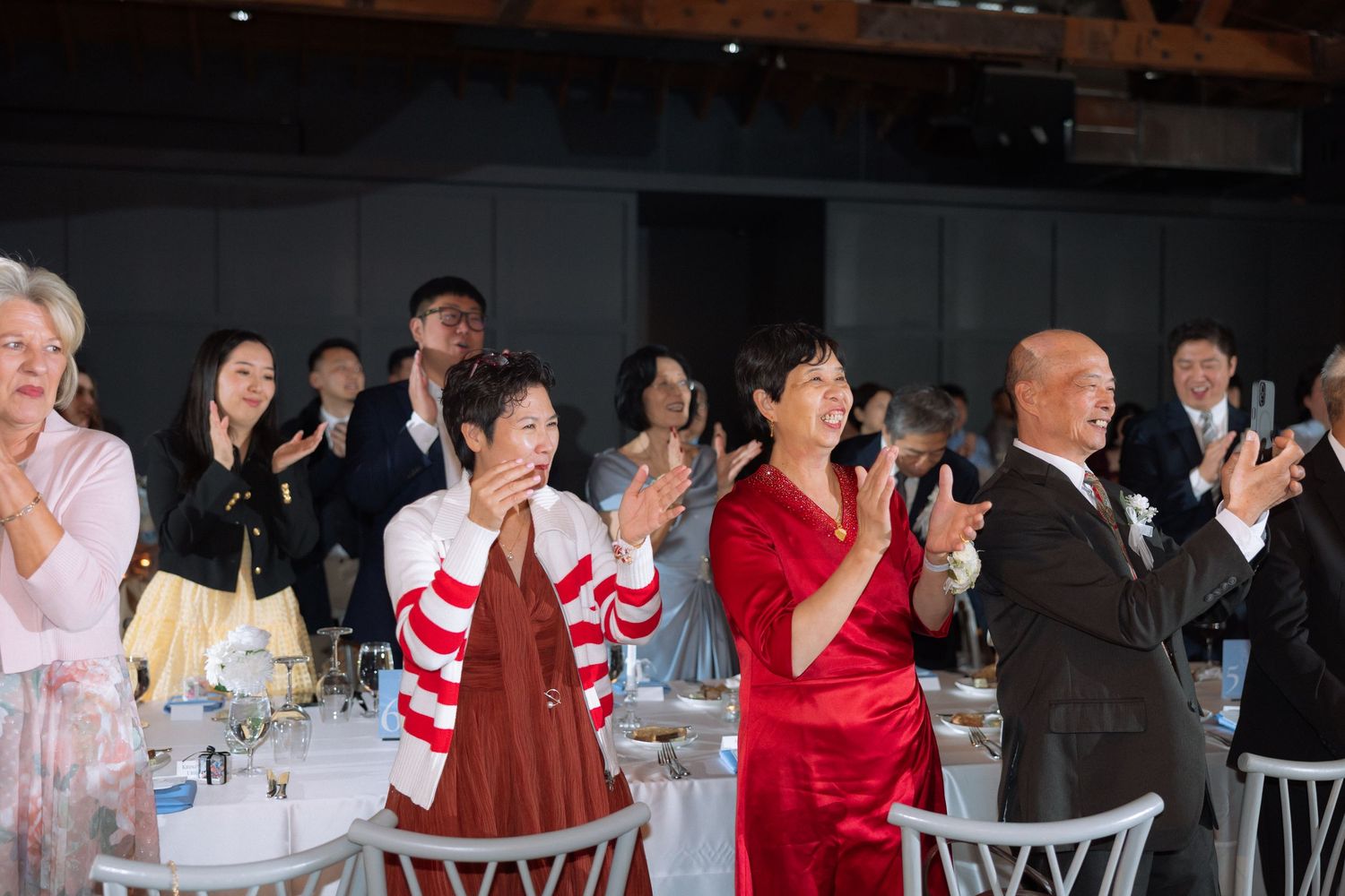 Guests clapping and celebrating at an elegant wedding reception dinner in a modern venue.
