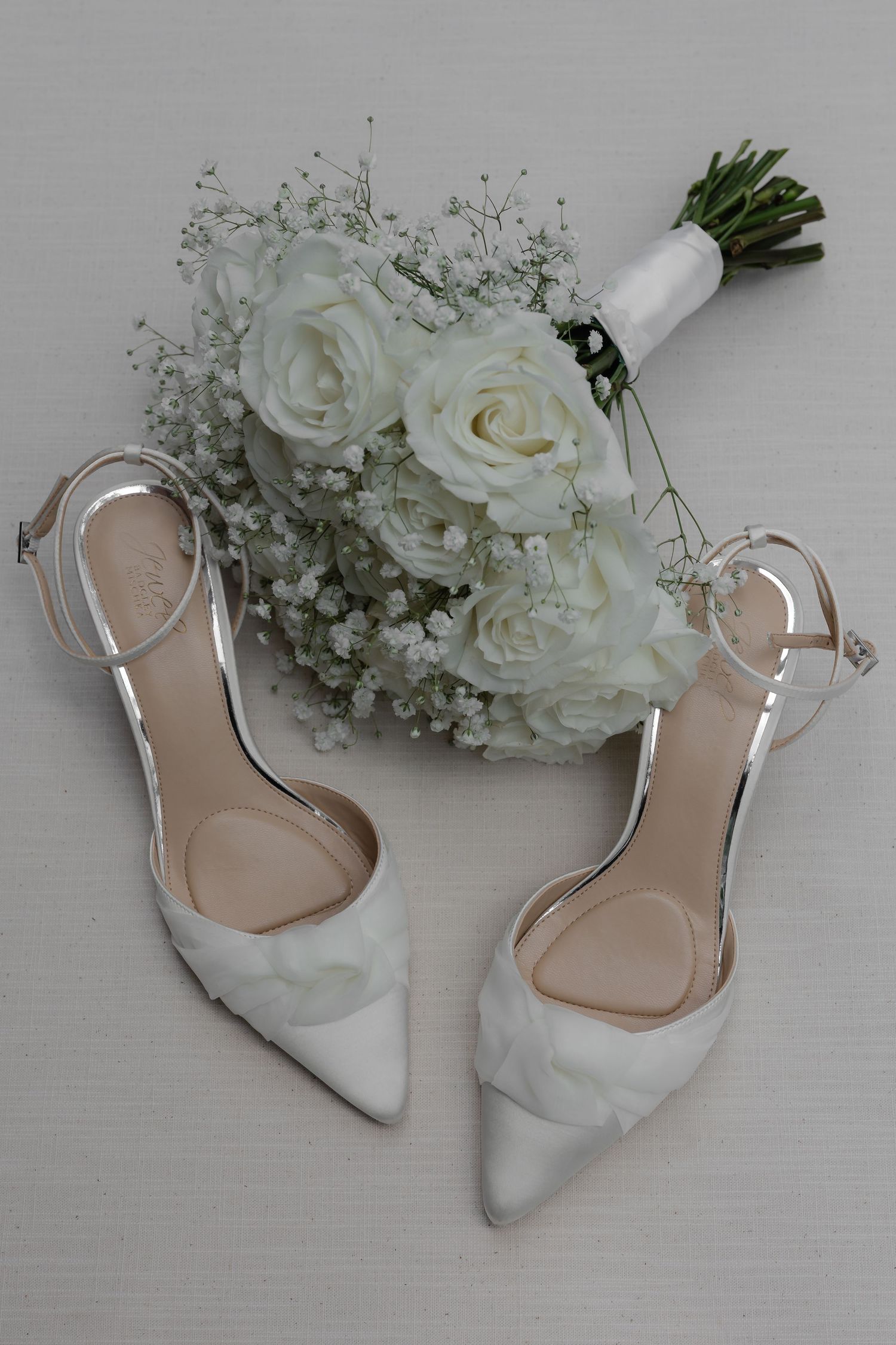 White wedding heels and bridal bouquet of roses and baby's breath on a light background.