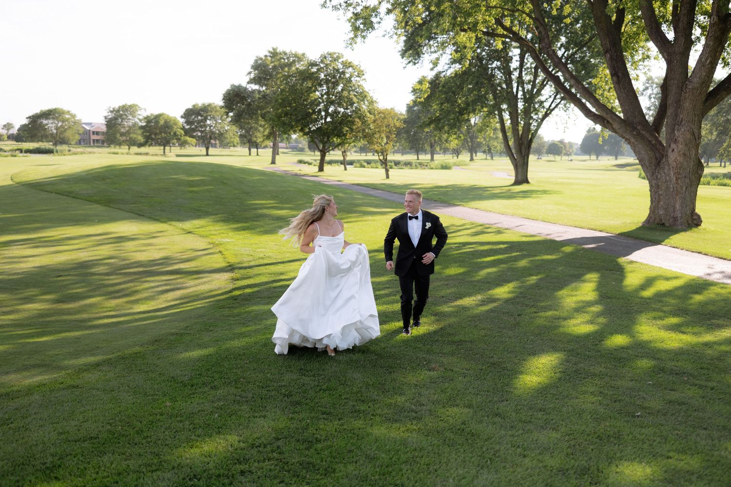 Bride and groom running joyfully across a lush green golf course on their wedding day.