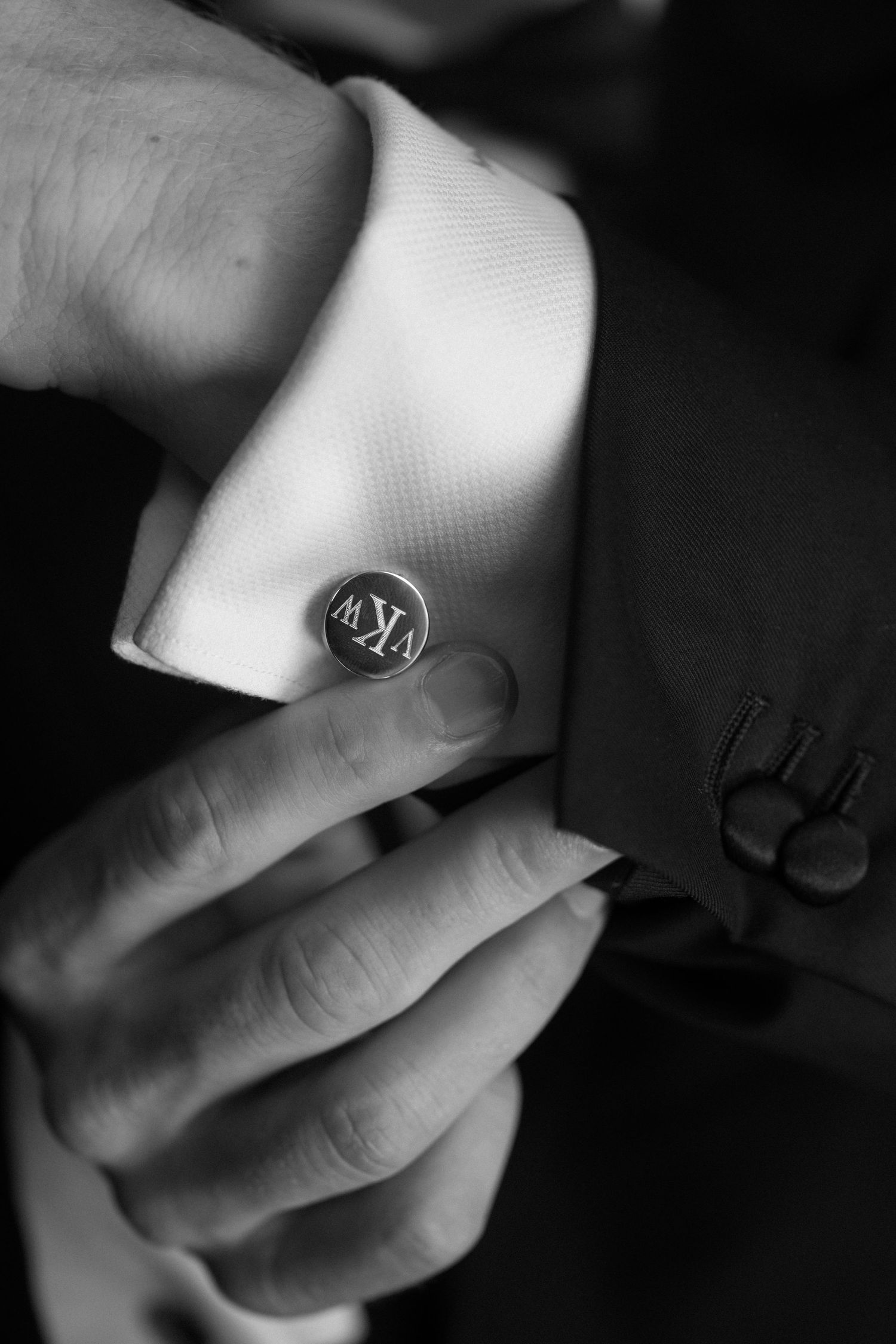 Close-up black and white photo of monogrammed cufflinks on groom's white dress shirt.