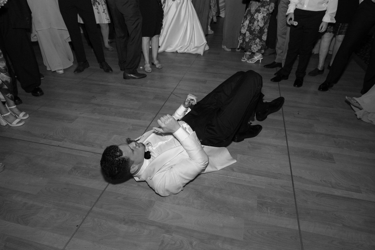 Wedding guest lying on the dance floor mid-performance at a lively reception celebration.