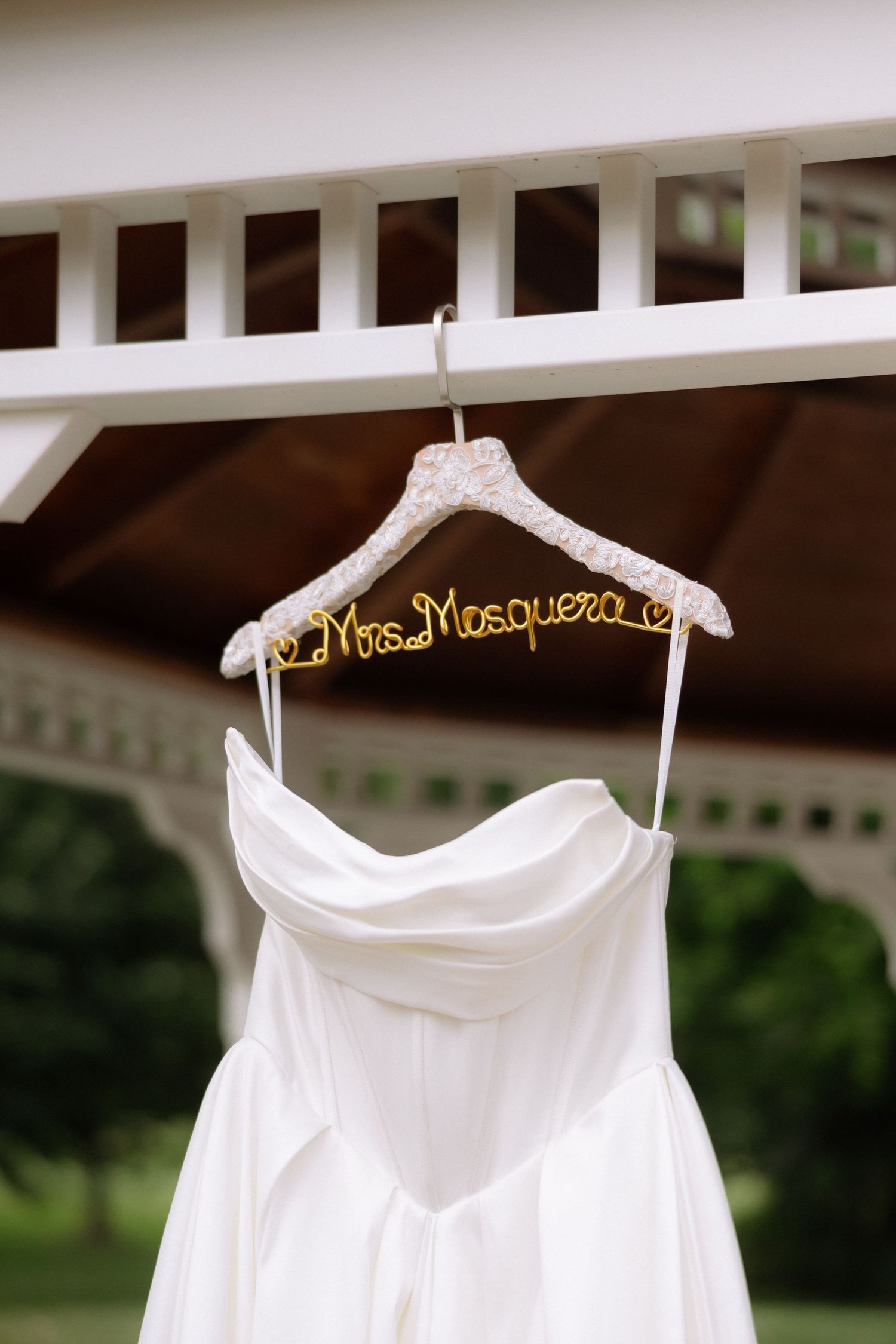 White strapless wedding dress hanging on custom Mrs. Mosquera hanger outdoors.