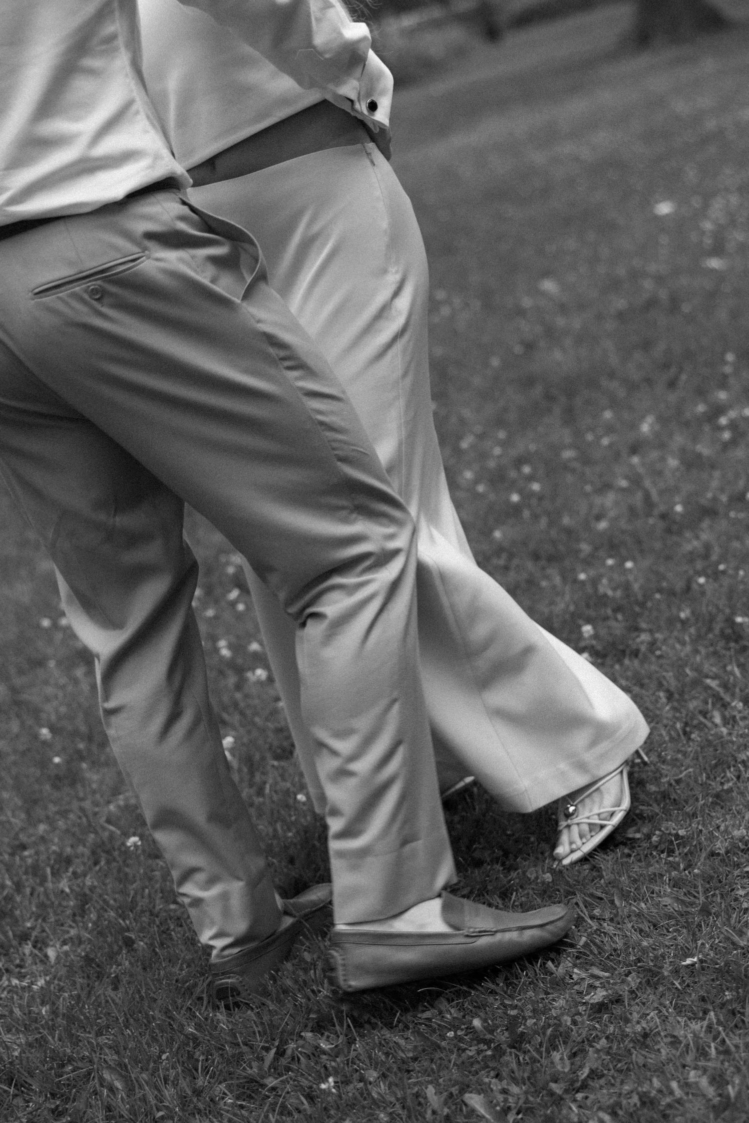 Black and white close-up of a man in khaki trousers and leather loafers dancing on a grass lawn.