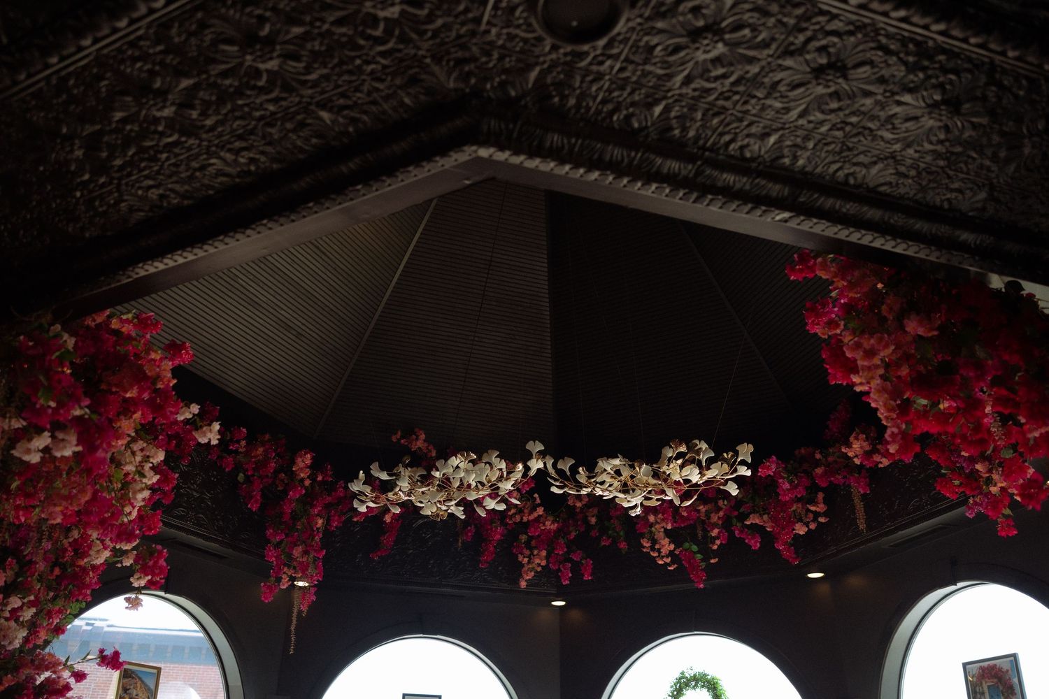 Red and white floral garlands hanging from a dark ornate ceiling in an elegant venue.