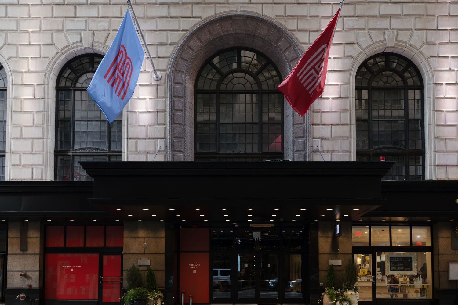 Grand hotel entrance with arched windows, Chicago and red flags flanking a classic stone facade at dusk.