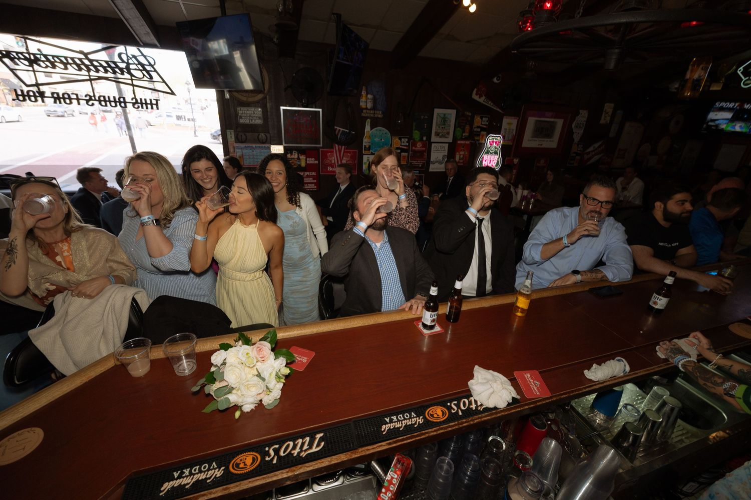 Group of people gathered at a bar counter, raising drinks and toasting together in a lively celebration.