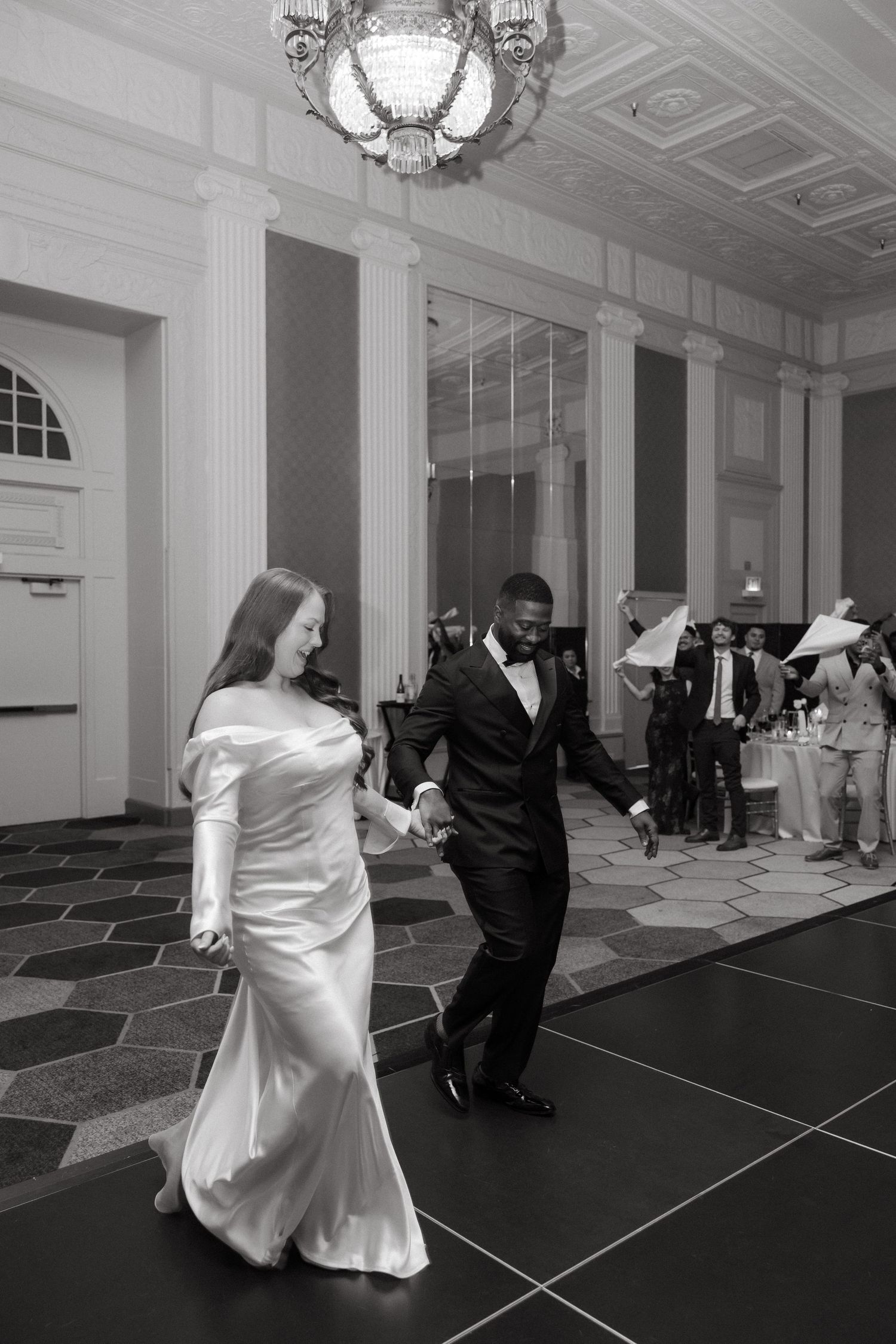 Black and white photo of a bride and groom sharing their first dance at an elegant wedding reception venue.
