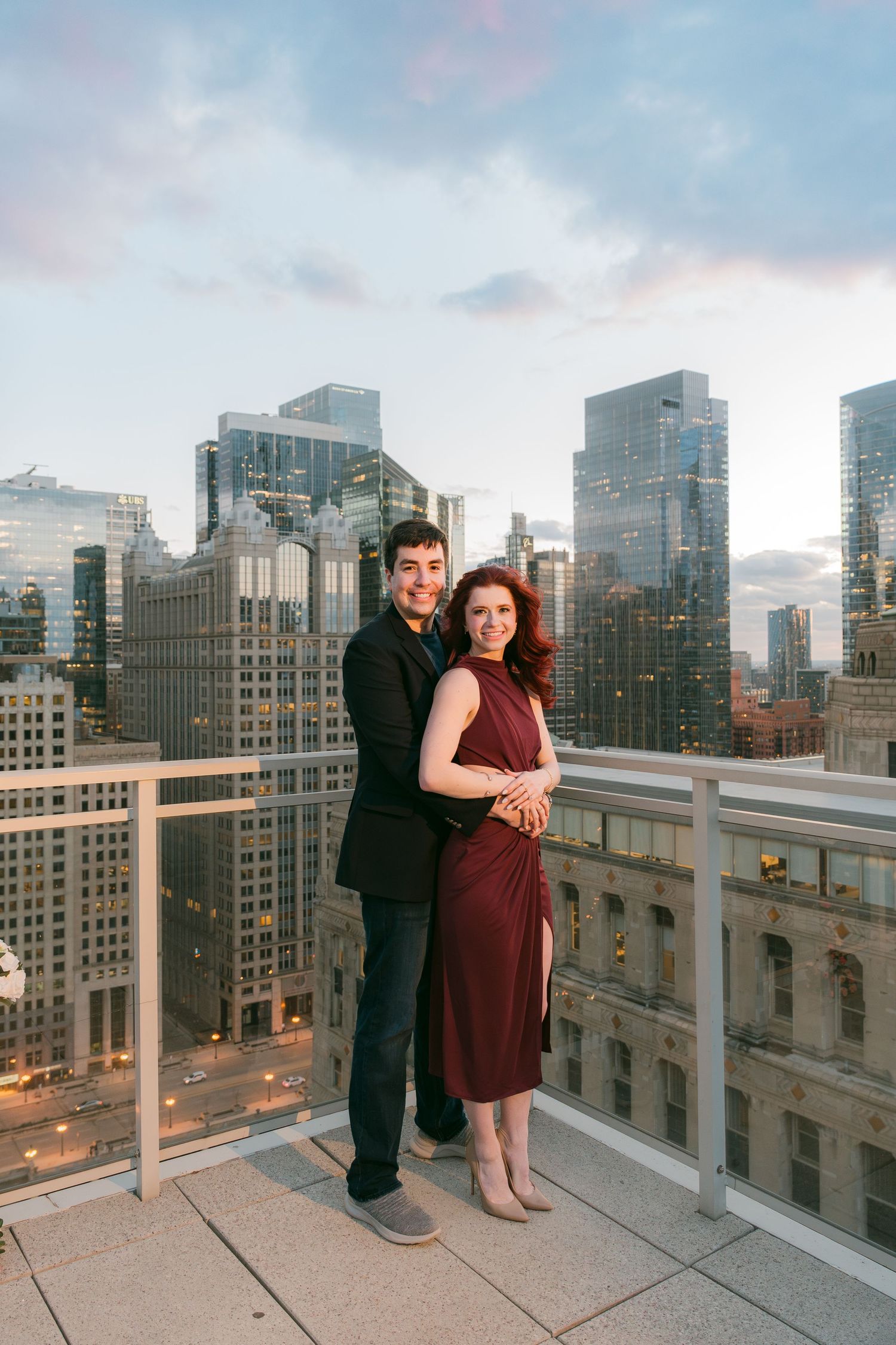 Smiling couple posing together on Chicago rooftop with glittering city skyline at dusk.