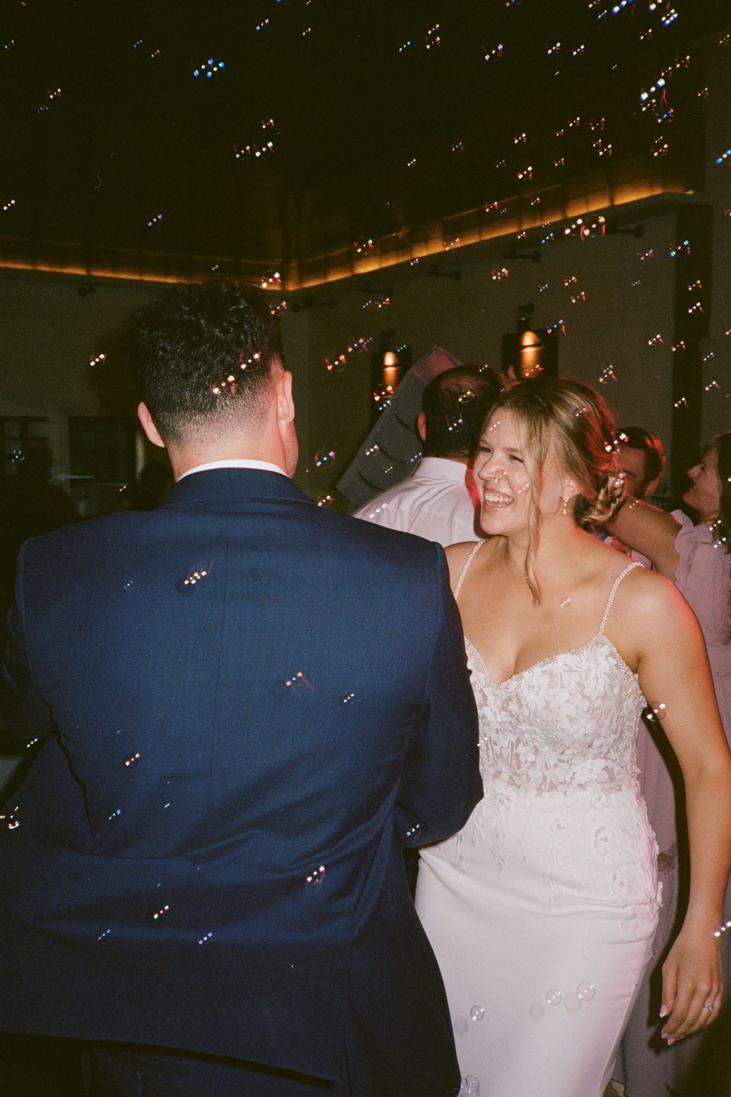 Bride and groom share a joyful first dance surrounded by floating bubbles at their wedding reception.