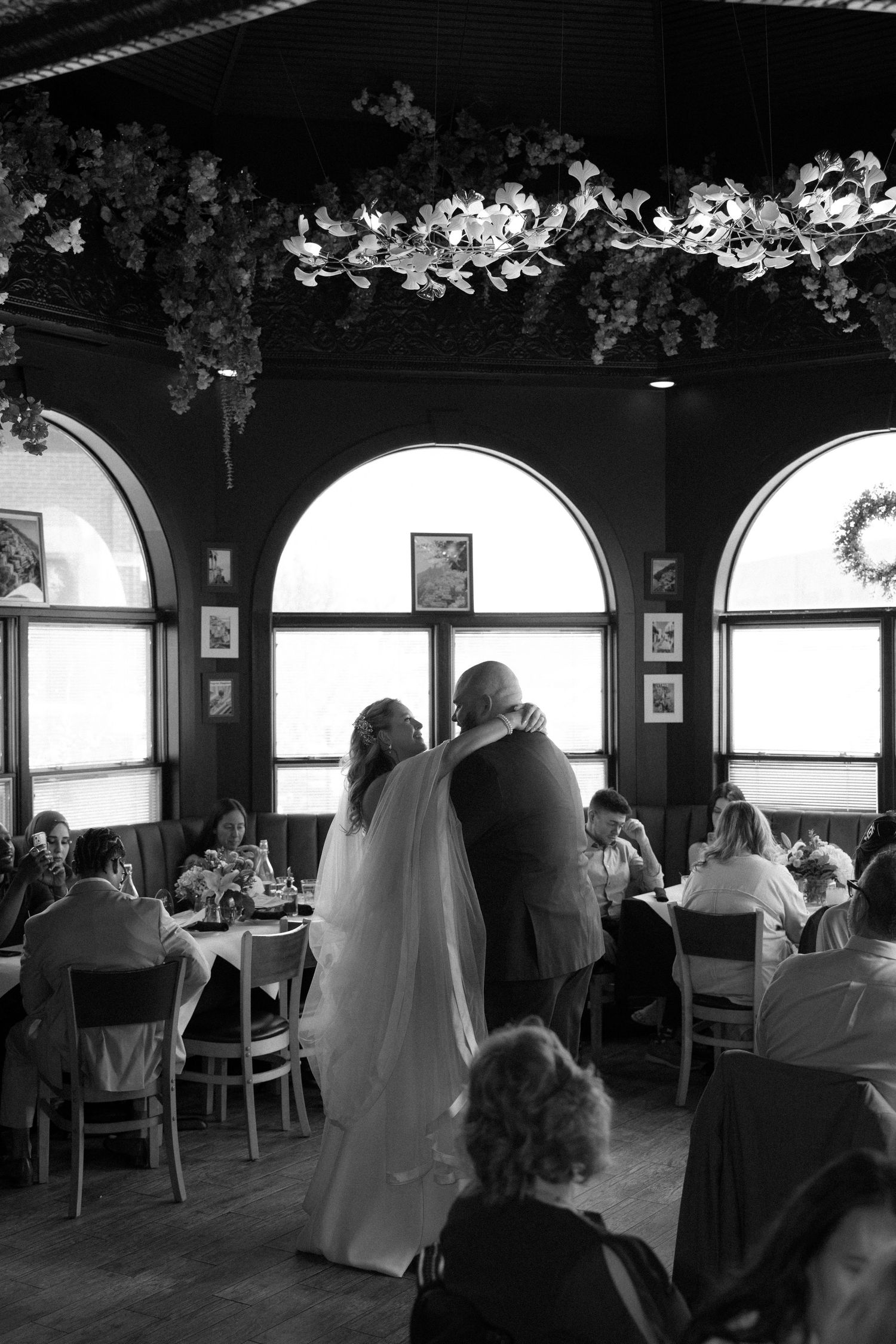 Black and white photo of a bride and groom sharing a dance at their wedding reception in an elegant restaurant venue.