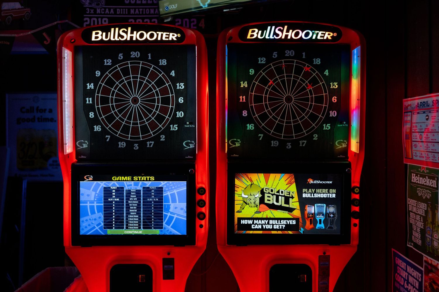 Two BullShooter electronic dartboard arcade machines glowing with red LED lights in a dimly lit game room.