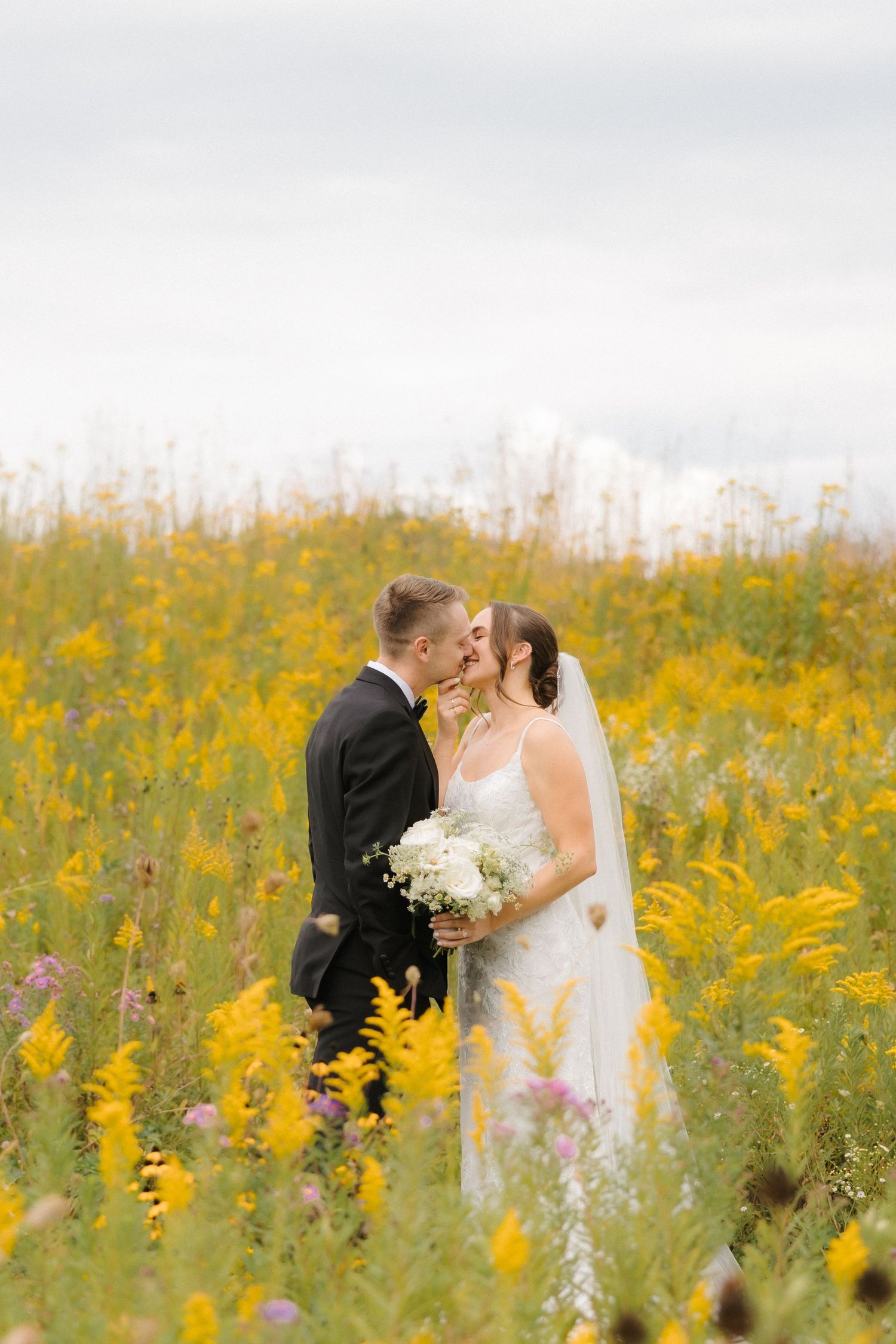 Bride and groom kissing in a vibrant yellow wildflower field, bride holding white bouquet.