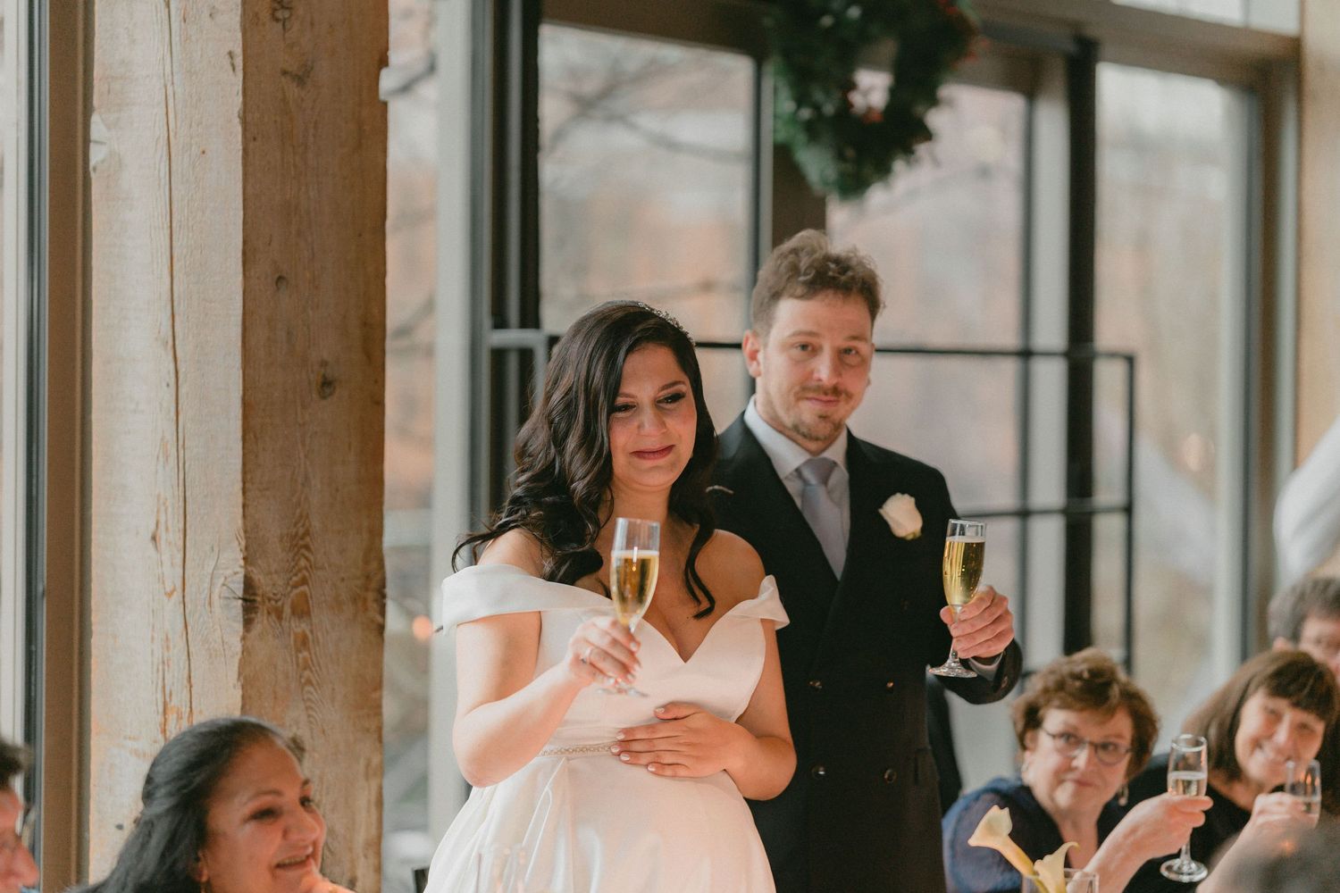 Bride and groom raising champagne glasses during wedding reception toast in a warmly lit venue.
