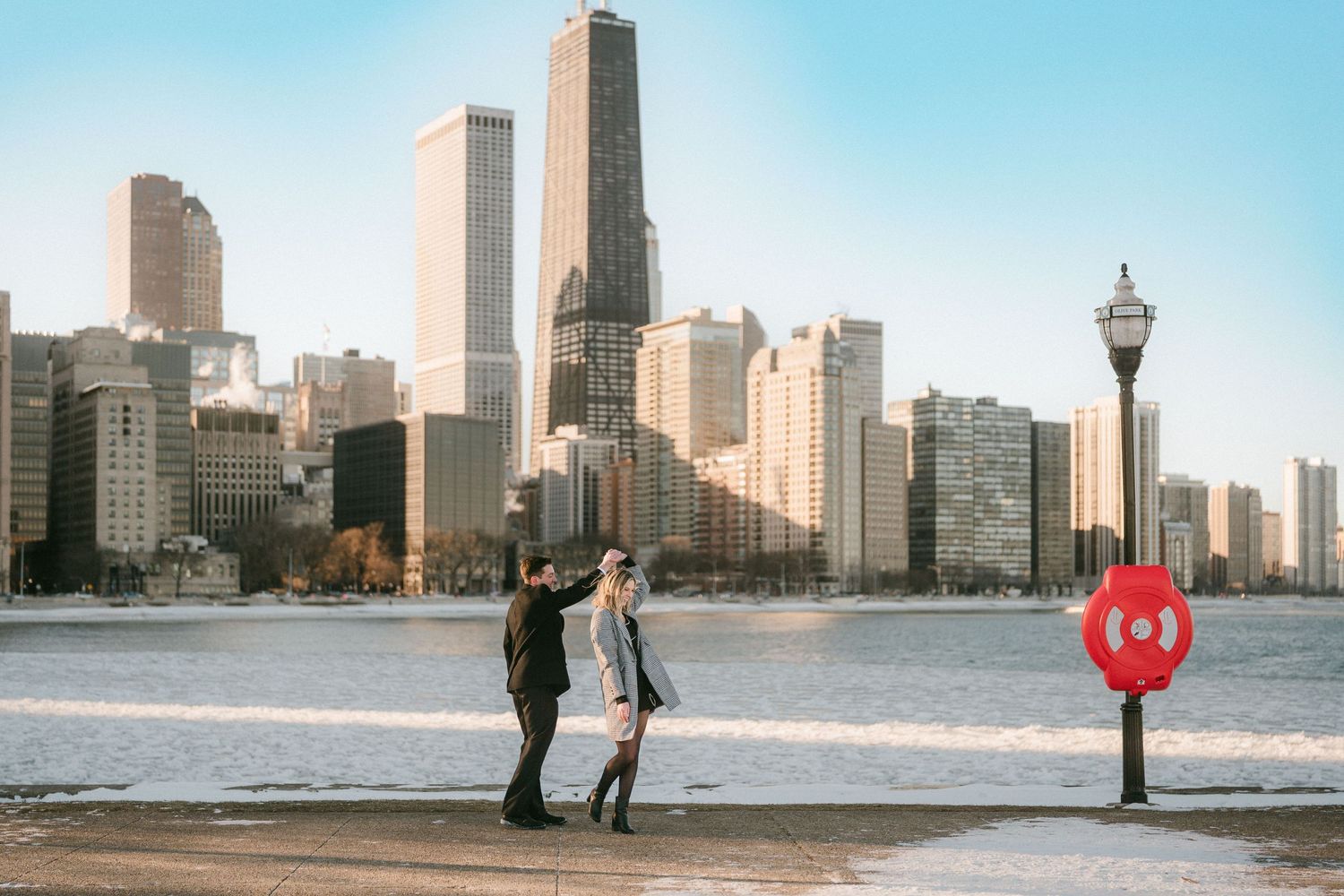 Couple walking along frozen Chicago lakefront with city skyline in background.
