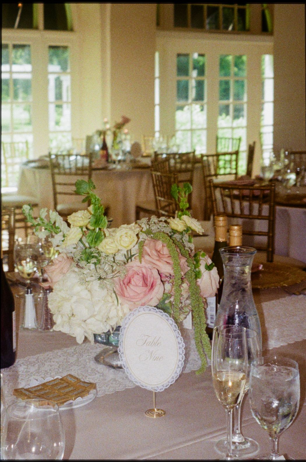 Elegant wedding reception table with pink and white floral centerpiece, champagne glasses, and lace details in a bright venue.