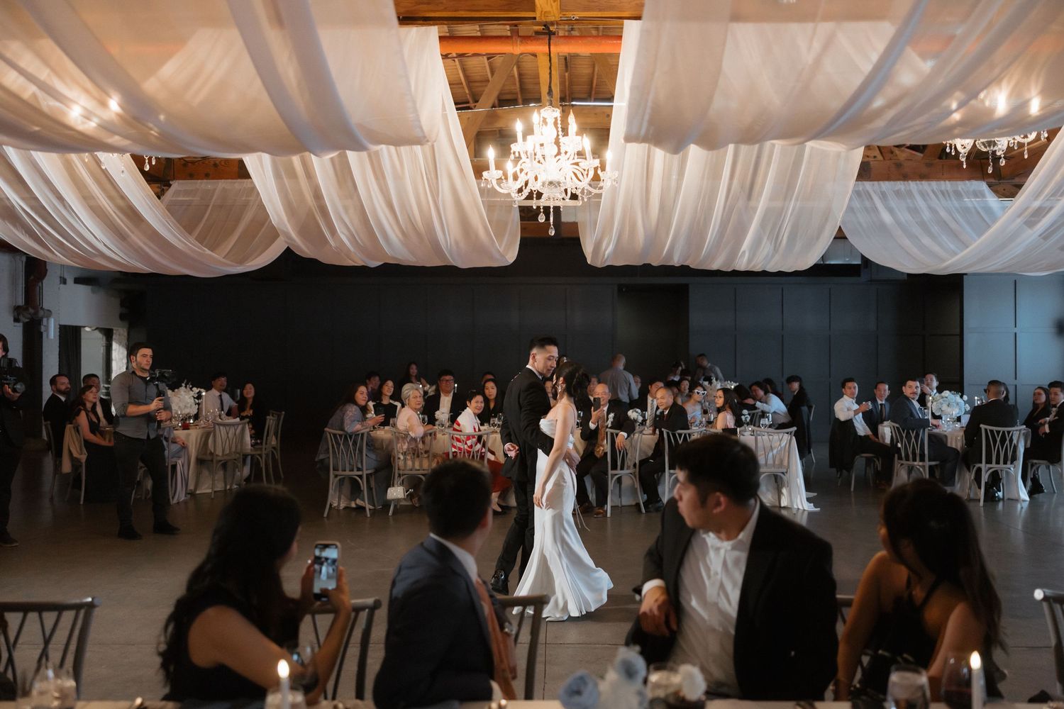 Bride and groom share their first dance at a romantic wedding reception with chandelier lighting.