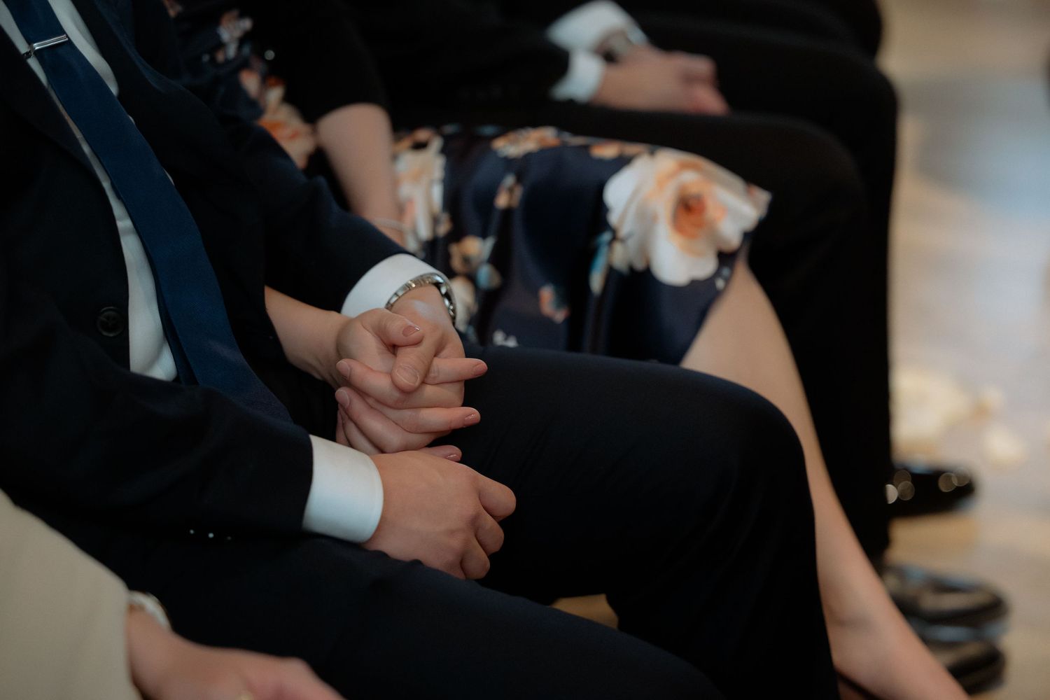 Close-up of wedding guests holding hands during an emotional indoor wedding ceremony.