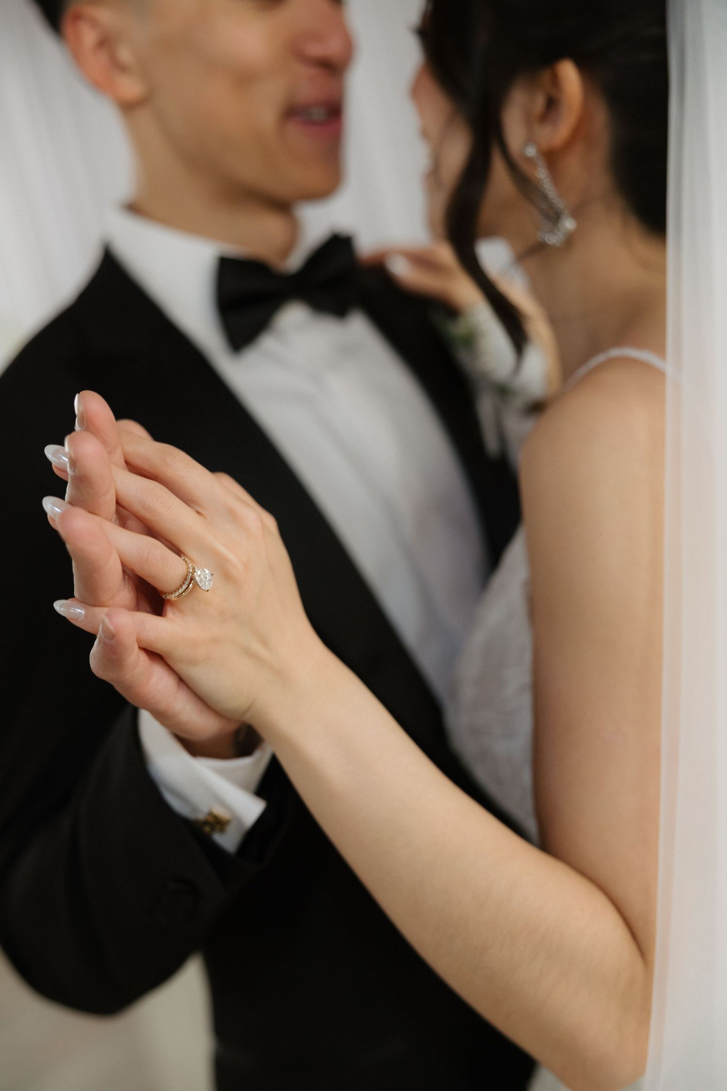 Bride and groom holding hands at wedding, showcasing elegant diamond engagement ring and manicured nails.
