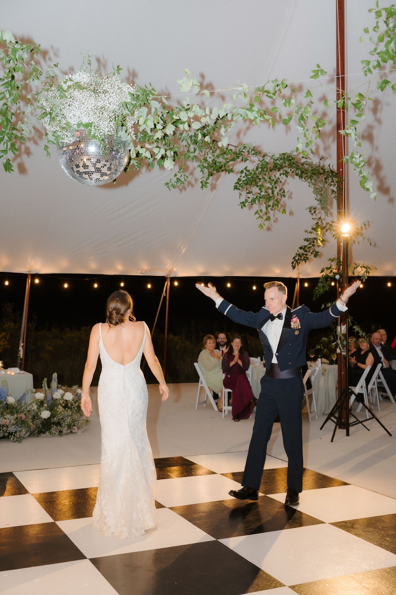 Groom in military uniform celebrates with bride on a black and white dance floor at their wedding.
