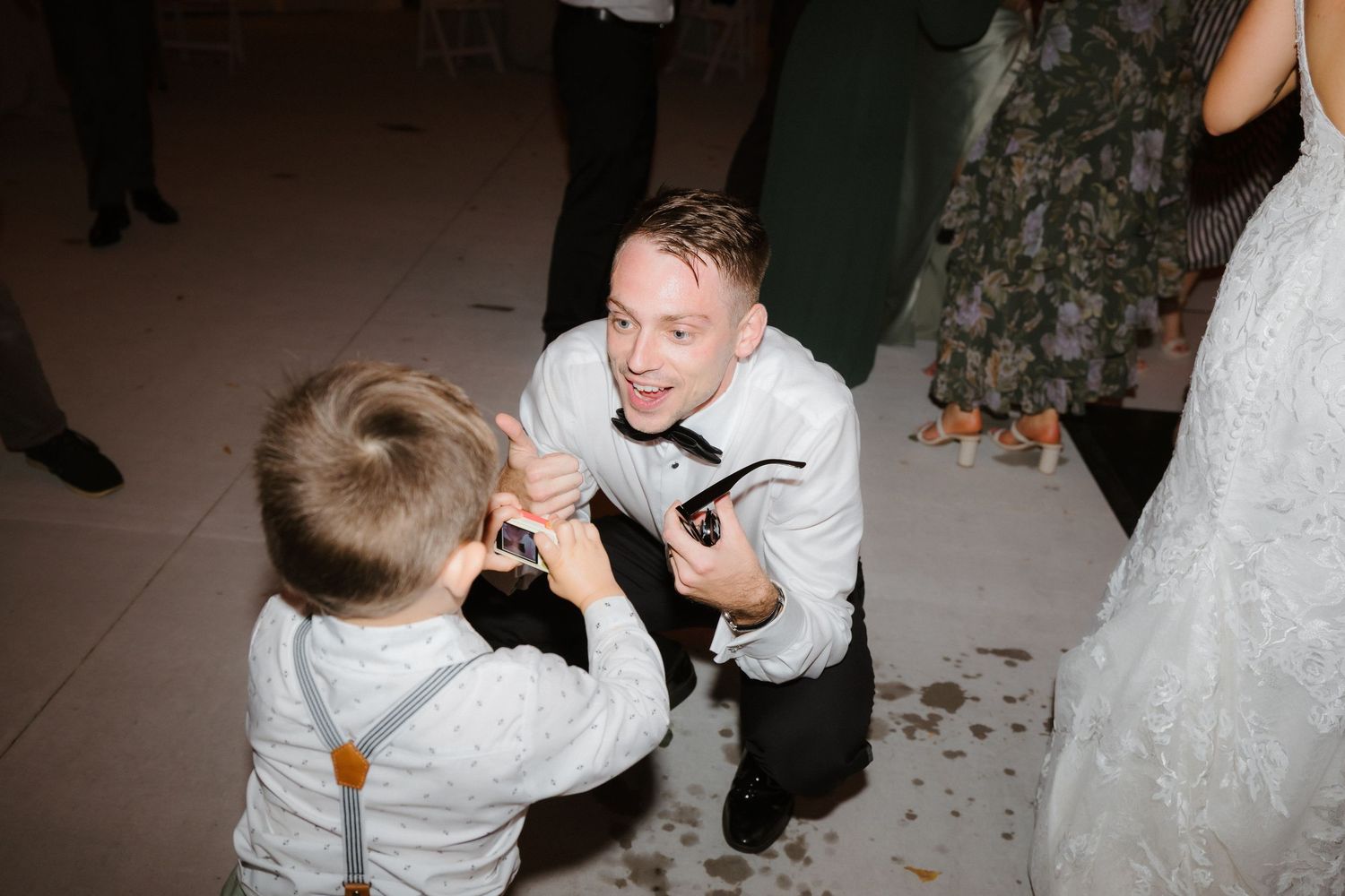 Groom kneels down to dance and interact with young child guest on the wedding reception dance floor.
