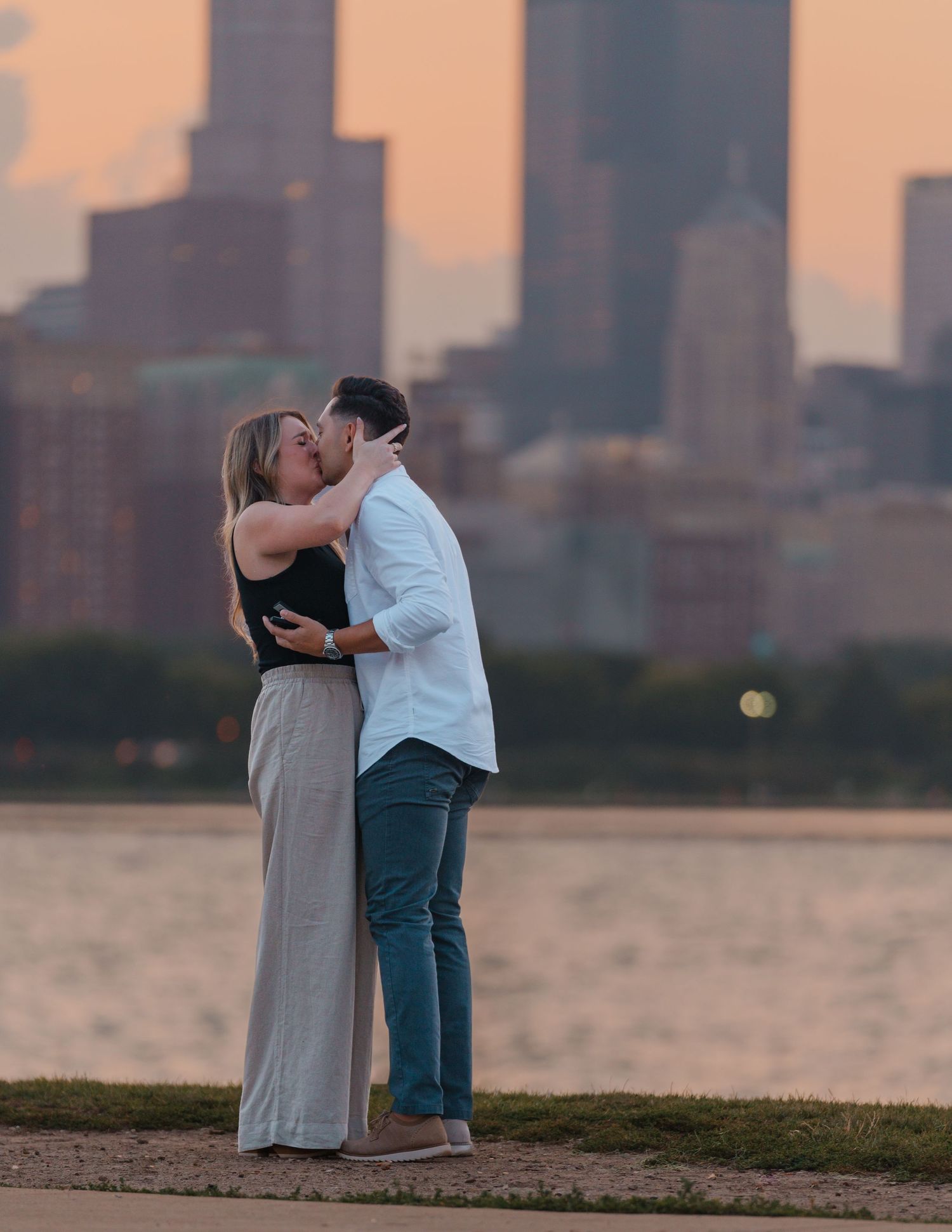 Newly engaged couple sharing a tender kiss by Lake Michigan with the Chicago skyline at sunset.