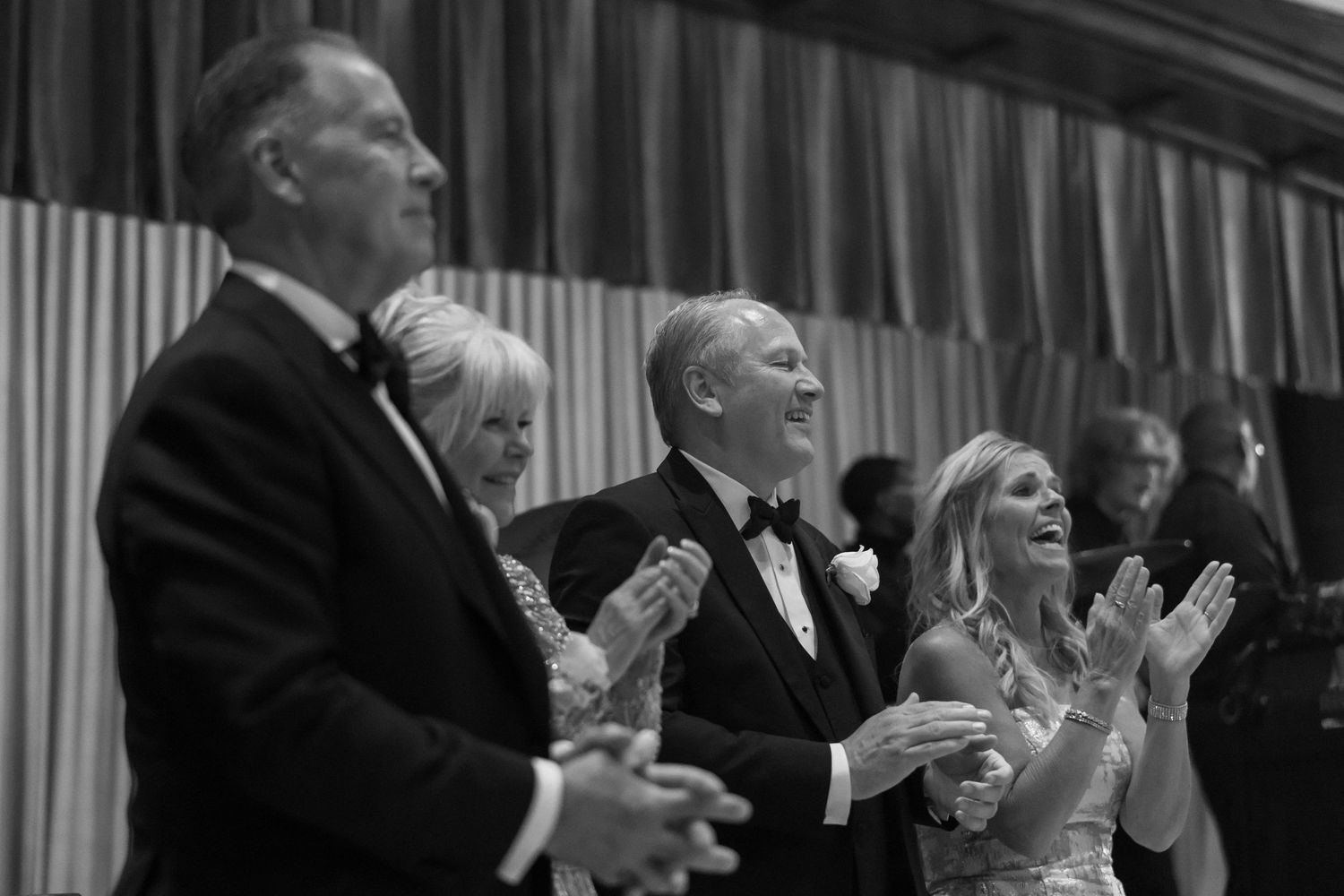 Joyful wedding guests clapping and laughing during a wedding reception celebration in black and white photo.