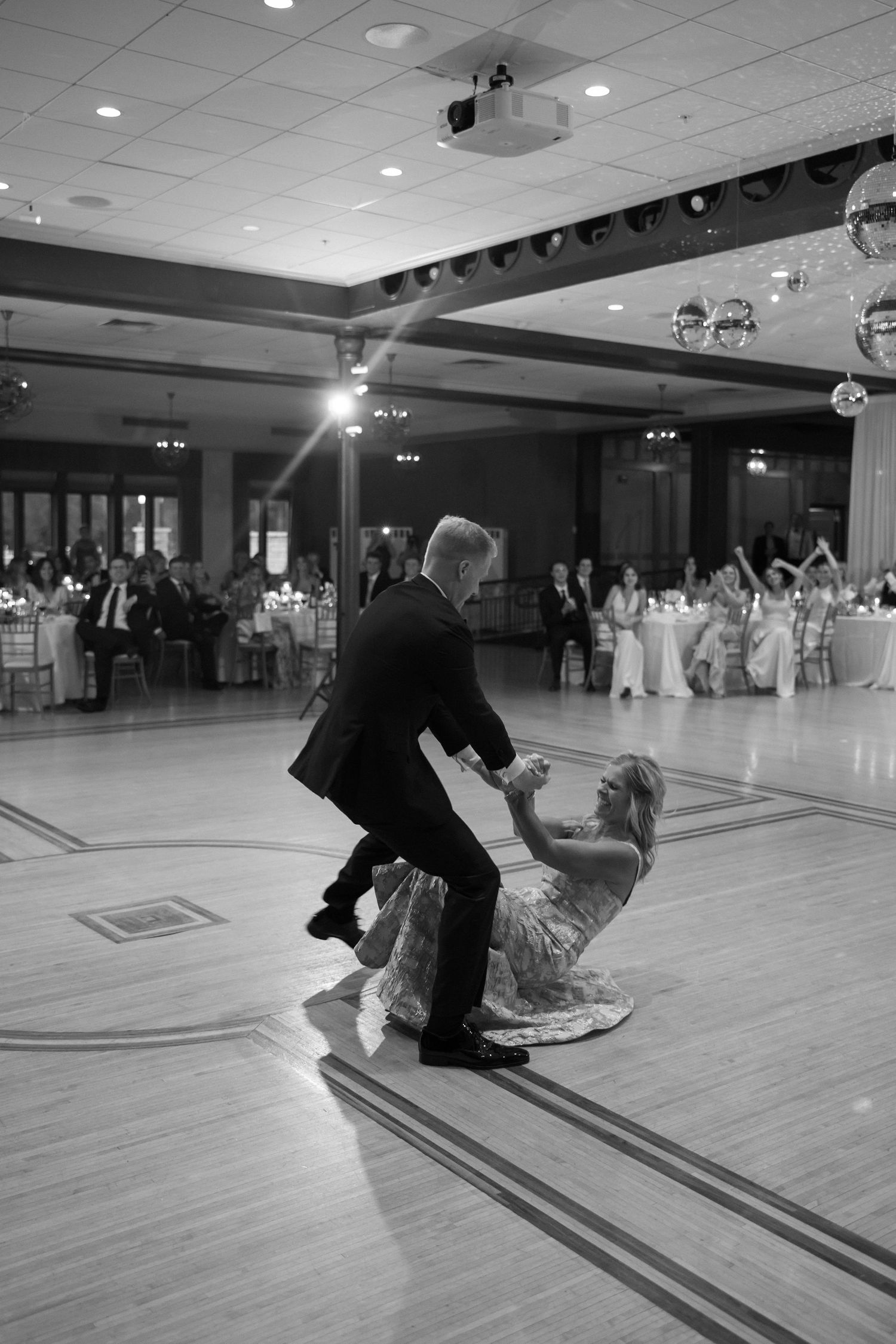 Couple performs dramatic dip on ballroom dance floor at elegant wedding reception.