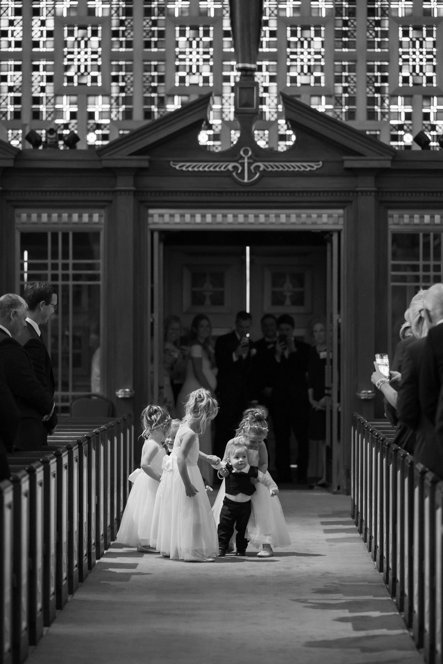 Adorable flower girls and ring bearer walking down the church aisle in black and white photo.