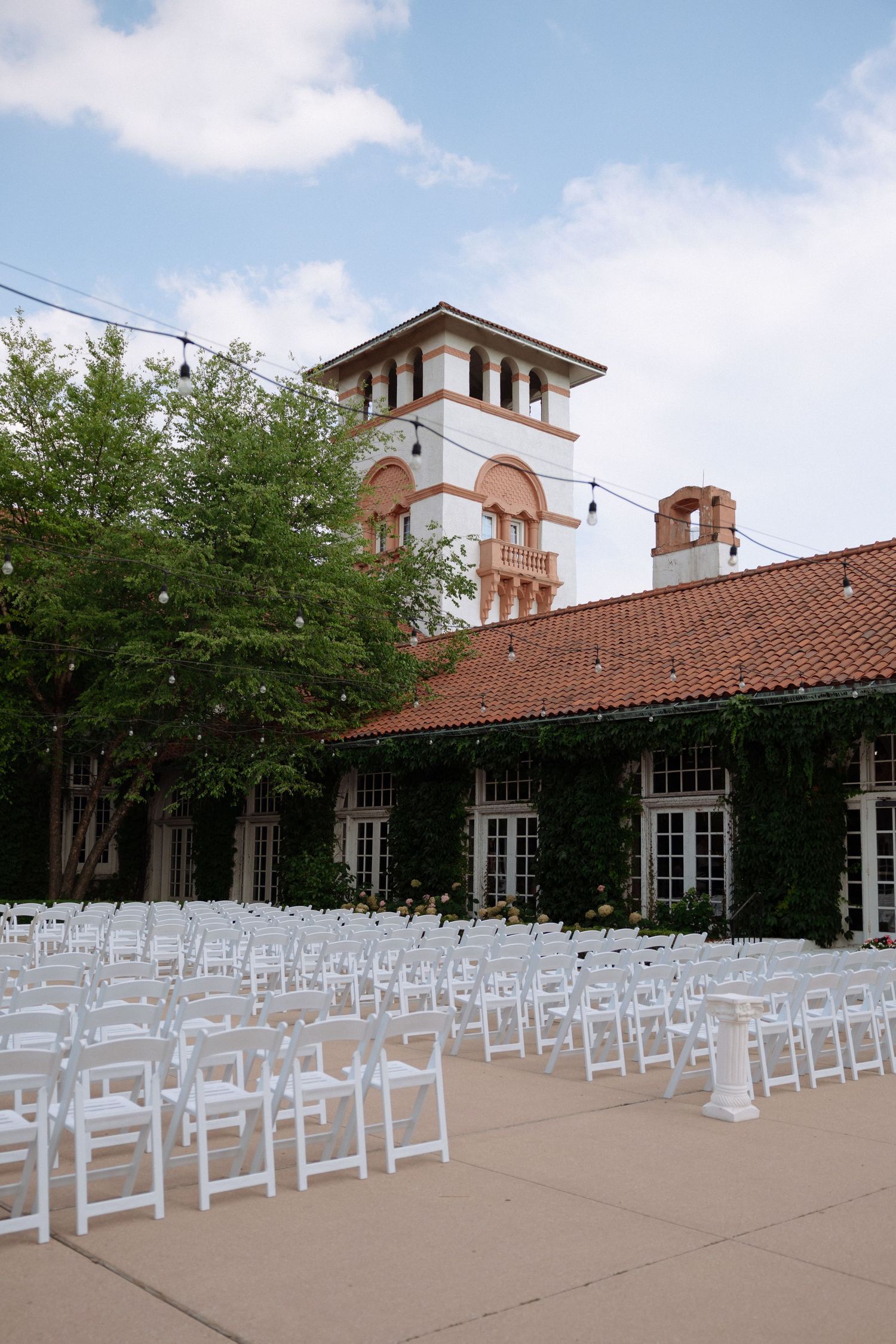 White folding chairs arranged in rows for an outdoor wedding ceremony at a Spanish-style venue with red tile roof.