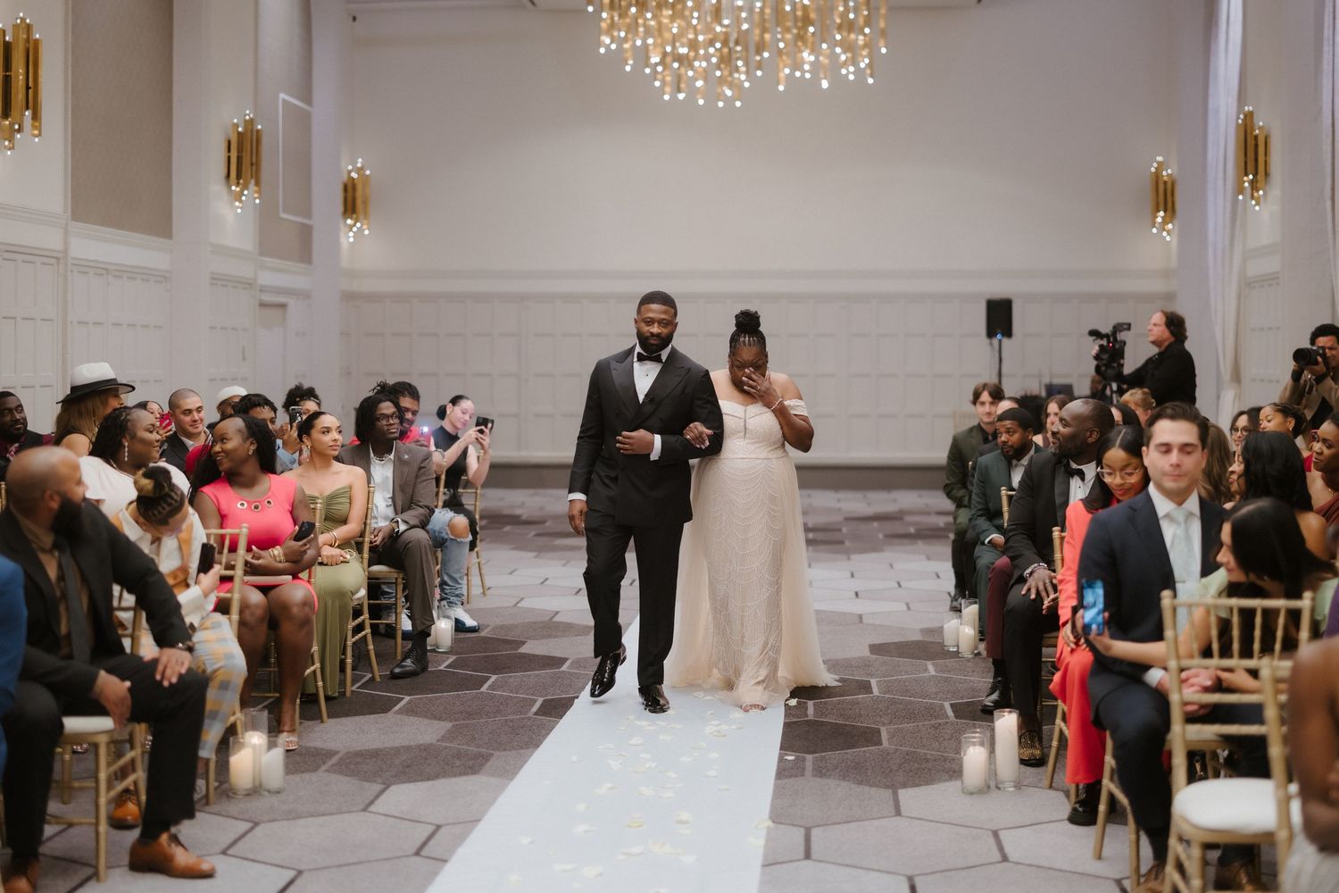 Bride and groom walk down the aisle together during elegant indoor wedding ceremony with chandeliers.