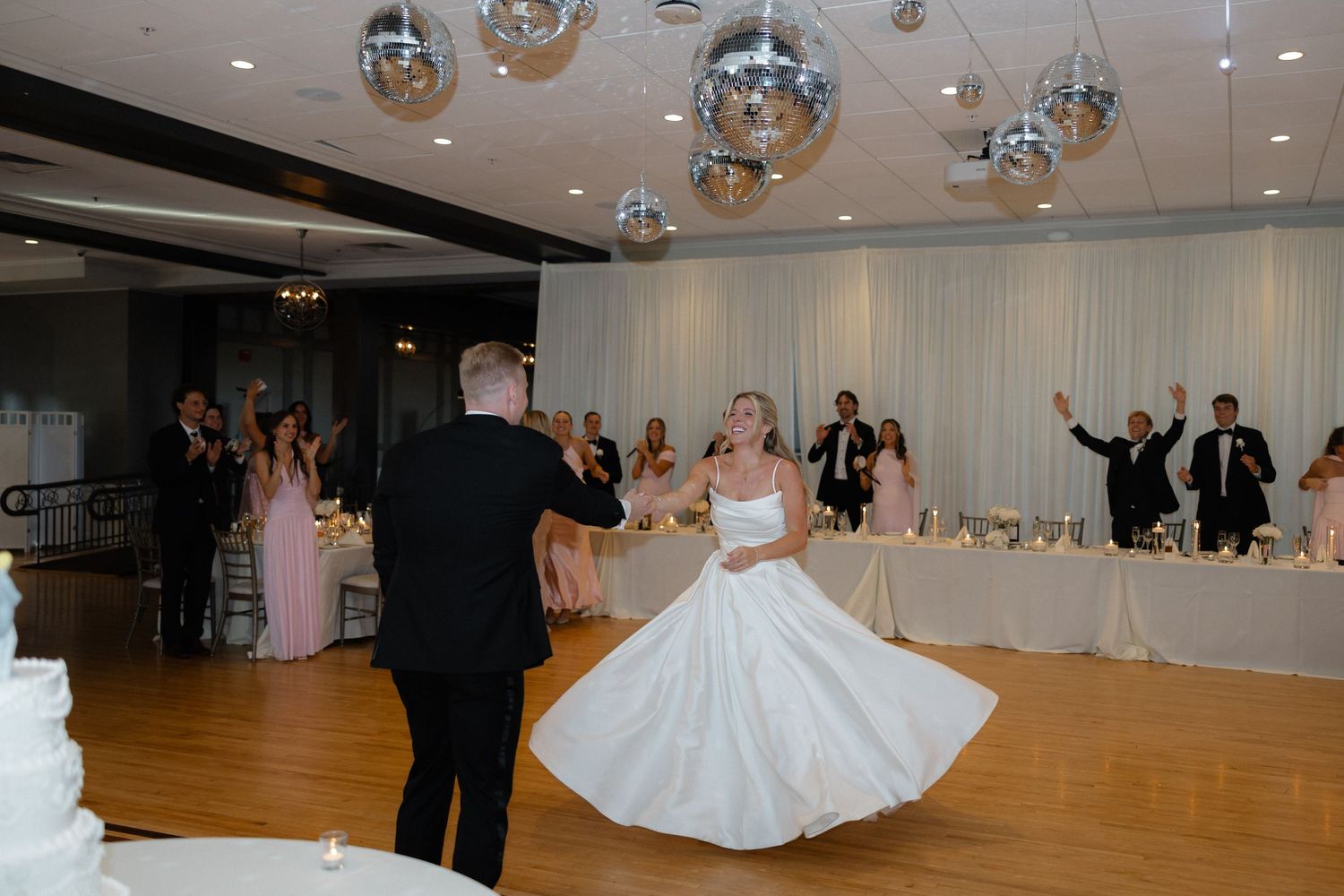 Bride and groom share first dance as guests cheer beneath silver disco balls in elegant reception venue.