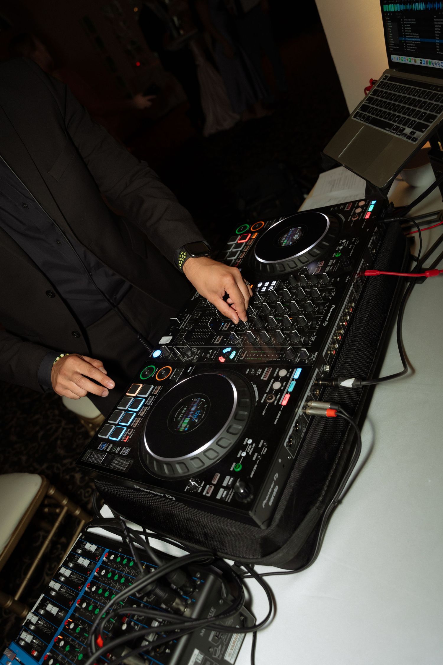 DJ mixing music on a professional controller with turntables and laptop at a wedding reception.