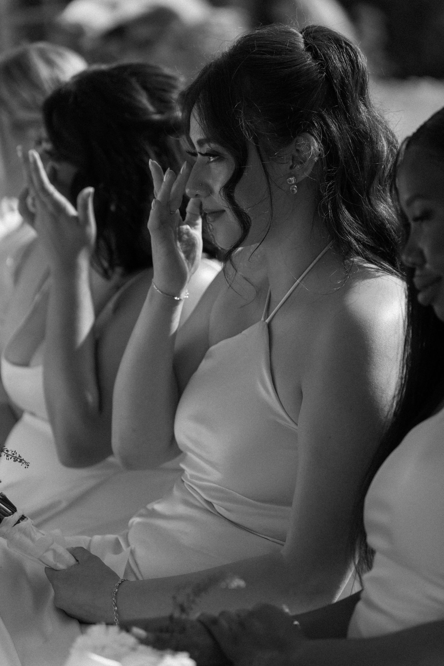 Emotional bridesmaid wiping tears during a wedding ceremony in this black and white portrait photo.