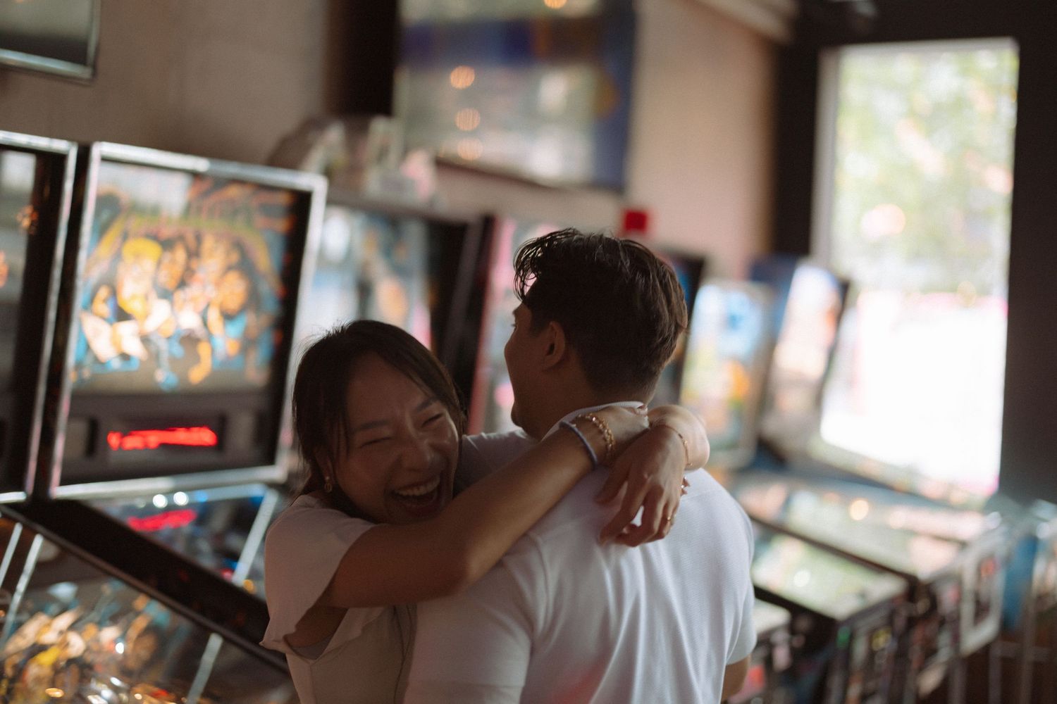 Happy couple embracing and smiling among colorful pinball machines in an arcade.